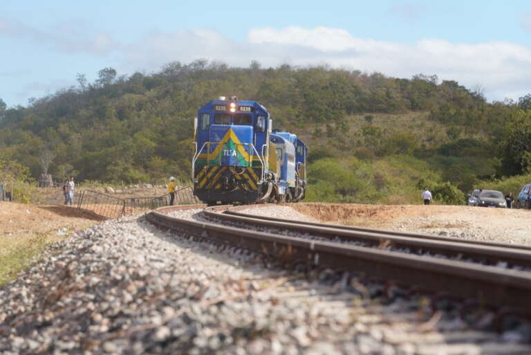 Como a Transnordestina está transformando o transporte de cargas no Nordeste? A ferrovia já transporta cargas reais, com 81% da fase 1 concluída. Em janeiro de 2026, transportou 946 toneladas de sorgo entre Piauí e Ceará em 16 horas e 34 minutos. Qual foi o impacto dos testes iniciais da Transnordestina? Os testes mostraram eficiência no transporte de cargas, com o primeiro teste em dezembro de 2025 transportando mil toneladas de milho em 12 horas e 46 minutos. Quais são os principais trechos da Transnordestina? A linha principal tem 1.206 km, ligando Eliseu Martins, no Piauí, ao Porto do Pecém, no Ceará, passando por 53 municípios em três estados. Qual é o investimento total na Transnordestina? O investimento estimado é de R$ 15 bilhões, com R$ 11,5 bilhões já aplicados. Em março de 2026, foram liberados R$ 152,4 milhões para o trecho entre Ceará e Piauí. Qual é o status atual da fase 1 da Transnordestina? A fase 1, entre Paes Landim e Pecém, está 81% concluída, com 727 km finalizados e 326 km em execução. A previsão de entrega é 2027. Como a chegada de trilhos da China impacta a obra? Em fevereiro, 33.900 toneladas de trilhos chegaram ao Pecém, essenciais para concluir a ferrovia e manter o cronograma de obras. Qual é o desafio do segmento final da Transnordestina? O trecho entre Caucaia e o Porto do Pecém é complexo, pois precisa ser integrado à infraestrutura portuária existente, exigindo obras paralelas. Como a Transnordestina afetará o Porto do Pecém? Com a ferrovia, o porto pode movimentar até 28 milhões de toneladas por ano, aumentando a eficiência e reduzindo custos de transporte. Por que o transporte ferroviário é mais econômico? O custo por tonelada-quilômetro no transporte ferroviário pode ser até quatro vezes menor que o rodoviário, essencial no Nordeste, onde 69% das rodovias são ruins. Quais são os benefícios dos terminais ao longo da ferrovia? Terminais em locais como Missão Velha e Iguatu permitem que cargas embarquem próximas à origem, reduzindo a dependência de caminhões. O que é o Porto Seco José Dias de Macêdo? É um terminal aduaneiro em Quixeramobim, com 362 hectares, que facilita o desembaraço de cargas no interior, reduzindo tempo e custos. Qual é a vantagem geográfica do Porto do Pecém? Está mais próximo da Europa e América do Norte do que portos do Sul e Sudeste, com travessias mais rápidas, como oito dias até a Espanha. Como a Transnordestina integra o interior produtor ao porto? A ferrovia conecta áreas agrícolas do Piauí e Ceará ao Porto do Pecém, melhorando a logística e competitividade das exportações. Qual é a importância da ligação com a Ferrovia Norte-Sul? Essa conexão estende o corredor até o Matopiba, região que responde por 19% da produção nacional de soja, impulsionando o agronegócio. Como a Transnordestina mudará o transporte de cargas em 2027? Com a conclusão da fase 1, o transporte que hoje leva dias de caminhão será feito em horas de trem, revolucionando a logística regional.