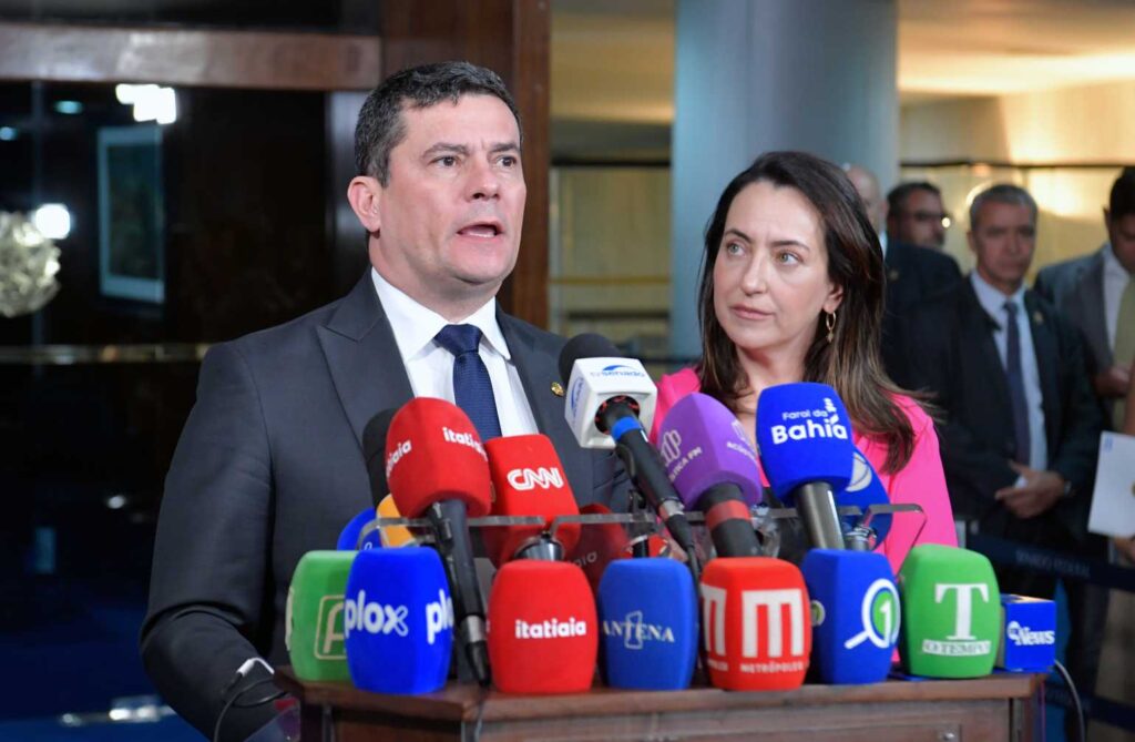 A **filiação de Sérgio Moro ao Partido Liberal (PL)** nesta terça-feira marca um momento significativo na política brasileira, confirmando uma **aliança estratégica com Flávio Bolsonaro**. Este movimento político ocorre em uma cerimônia em Brasília, que também contará com a filiação de Rosangela Moro, esposa do ex-juiz e atual deputada. Mas o que essa filiação representa para o cenário político brasileiro? Por que Sérgio Moro decidiu se filiar ao PL? A decisão de Moro de se juntar ao PL pode ser vista como uma tentativa de fortalecer sua posição política e ampliar sua base de apoio. O PL é um partido com forte presença no cenário político nacional, e a filiação de Moro pode indicar uma estratégia para consolidar alianças e aumentar sua influência nas próximas eleições. Qual é o impacto da aliança com Flávio Bolsonaro? A **aliança com Flávio Bolsonaro**, filho do ex-presidente Jair Bolsonaro, sugere uma aproximação com o grupo político que ainda mantém uma base significativa de apoio no Brasil. Essa parceria pode ser vista como uma tentativa de unir forças entre figuras proeminentes da política brasileira, potencialmente criando um bloco político mais robusto e influente. O que a filiação de Rosangela Moro ao PL significa? A filiação de Rosangela Moro ao PL, além de fortalecer a presença do casal no partido, pode indicar uma estratégia conjunta para aumentar a visibilidade e a influência política da família Moro. Como deputada, Rosangela já possui um papel ativo na política, e sua adesão ao PL pode ser vista como um passo para alinhar suas ações políticas com as de seu marido. Quais são as implicações para as eleições de 2026? Com a filiação de Moro e sua esposa ao PL, o partido pode estar se preparando para desempenhar um papel significativo nas **eleições de 2026**. A presença de figuras conhecidas e influentes como Sérgio e Rosangela Moro pode atrair mais eleitores e fortalecer a posição do PL no cenário político nacional. Como essa movimentação afeta o panorama político no Paraná? No contexto do Paraná, estado de origem de Sérgio Moro, essa filiação pode ter um impacto considerável. Moro já possui uma base de apoio significativa no estado, e sua aliança com o PL pode consolidar ainda mais sua posição, influenciando o cenário político local e potencialmente afetando as eleições estaduais. Quais são os desafios que Moro pode enfrentar com essa nova aliança? Apesar das vantagens potenciais, a aliança com Flávio Bolsonaro e o PL também pode apresentar desafios. A política brasileira é conhecida por sua volatilidade, e alianças podem ser tanto uma fonte de força quanto de vulnerabilidade. Moro precisará navegar cuidadosamente pelas complexidades políticas para manter o apoio de sua base e expandir sua influência. Em resumo, a **filiação de Sérgio Moro ao PL** e a confirmação de sua aliança com Flávio Bolsonaro representam um movimento estratégico importante no cenário político brasileiro. Com a adesão de Rosangela Moro ao partido, o casal fortalece sua presença política, preparando-se para influenciar as próximas eleições e consolidar sua posição no cenário nacional.