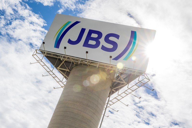 A **JBS** registrou um lucro líquido de **US$ 415 milhões** no quarto trimestre de 2025, mantendo-se praticamente estável em relação ao mesmo período do ano anterior. No acumulado do ano, o lucro totalizou **US$ 2,0 bilhões**, representando um aumento de 15% em comparação com 2024, conforme divulgado no balanço da empresa. A **receita líquida** da JBS atingiu um recorde de **US$ 23,06 bilhões**, superando as expectativas dos analistas, que previam **US$ 22,38 bilhões**. Este crescimento foi impulsionado por vendas historicamente altas nas operações de carne bovina na América do Norte e no Brasil. Apesar do aumento na receita, o **Ebitda ajustado** (lucro antes de juros, impostos, depreciações e amortizações) caiu 7% no trimestre, totalizando **US$ 1,72 bilhão**. Este declínio foi principalmente devido à alta nos custos do gado nos Estados Unidos. No acumulado de 2025, o Ebitda ajustado somou **US$ 6,8 bilhões**, uma queda de 5% em relação ao ano anterior. A **margem Ebitda ajustada** também diminuiu 1,8 ponto percentual, situando-se em 7,4%. O Conselho de Administração da JBS aprovou o pagamento de **dividendos** de **US$ 1 por ação**, a serem pagos em 17 de junho de 2026. Os acionistas que constarem na base acionária ao final do pregão de 18 de maio de 2026 terão direito a receber esses dividendos. A operação da **JBS Beef North America** enfrentou desafios devido à forte alta nos preços do gado e à menor oferta de animais, o que pressionou as margens, apesar da demanda resiliente no mercado norte-americano. No Brasil, a **JBS Brasil** destacou-se positivamente, com um crescimento de 26% na receita no quarto trimestre e 21% no ano. Este desempenho foi apoiado por preços mais altos, recorde de volume de abates, forte demanda externa e um bom desempenho no mercado doméstico, especialmente no último trimestre, favorecido pela demanda por cortes para churrasco. A **Seara** também apresentou crescimento nas vendas, impulsionada por maiores volumes e preços, além de um avanço no mercado doméstico e recorde de exportações, mesmo enfrentando restrições pontuais em alguns mercados internacionais ao longo do ano. Na **Austrália**, a JBS se beneficiou de preços mais elevados e ganhos de eficiência operacional, conseguindo compensar a alta nos custos do gado e ampliar suas margens. A **geração de caixa livre** da JBS foi de **US$ 990 milhões** no quarto trimestre, enquanto no acumulado de 2025 somou **US$ 400 milhões**. A alavancagem, medida pela relação dívida líquida sobre Ebitda ajustado, encerrou o período em 2,39 vezes, alinhada com o objetivo financeiro de longo prazo da companhia. Segundo o CEO global, Gilberto Tomazoni, a empresa encerrou o ano com um **retorno sobre patrimônio (ROE)** de 25% e um **retorno sobre o capital investido (ROIC)** de 17%, reforçando a disciplina financeira e a resiliência do modelo de negócios da JBS.