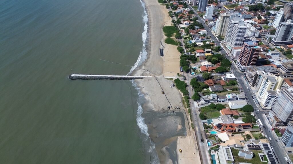 Qual é o objetivo da obra de alargamento na Praia de Balneário Piçarras? A obra visa ampliar a faixa de areia para combater a erosão e oferecer uma orla mais estruturada e segura, pronta para o futuro. Quanto já foi investido na obra de alargamento da praia? O investimento total já ultrapassa R$ 50 milhões, com R$ 9,57 milhões destinados à etapa adicional. Qual é o status atual da obra de alargamento? A primeira fase está 97% concluída, com previsão de entrega até 3 de abril. Qual é a extensão da nova faixa de areia? A nova extensão prevista é de aproximadamente 430 metros, com 180 metros já realizados. Por que a ampliação foi necessária? Estudos técnicos indicaram maior vulnerabilidade à erosão na área, justificando a ampliação. Quem conduziu os estudos técnicos para a obra? Os estudos foram conduzidos por instituições especializadas, como o Instituto Nacional de Pesquisas Hidroviárias. Qual é o papel da draga Amazone na obra? A draga Amazone transporta cerca de 6 mil metros cúbicos de areia por ciclo, realizando até quatro operações diárias. De onde é retirada a areia utilizada na obra? A areia é retirada a aproximadamente 10,5 km da costa, nas proximidades da Ponta da Vigia. A areia utilizada é semelhante à original da praia? Sim, a areia possui características semelhantes à original, garantindo a harmonia visual. Quantos metros cúbicos de areia já foram depositados na orla? Mais de 493 mil metros cúbicos de areia já foram depositados na orla. Como os moradores podem acompanhar o andamento das obras? Os moradores podem observar o andamento das obras através de um link do YouTube. Qual é a importância do planejamento e execução eficiente na obra? O ritmo acelerado da obra demonstra a eficiência do planejamento e execução, garantindo entrega no prazo. Como a obra impacta a segurança e estrutura da orla? A obra visa entregar uma orla mais ampla, estruturada e preparada para o futuro, com foco na segurança. Qual é a expectativa do prefeito de Balneário Piçarras sobre a obra? O prefeito Tiago Baltt destaca a responsabilidade ambiental e a continuidade dos trabalhos como fundamentais. Quais são as consequências da obra para a comunidade local? A obra promete melhorar a infraestrutura, combater a erosão e aumentar a segurança para moradores e turistas. Como a obra de alargamento pode beneficiar o turismo na região? Com uma orla mais ampla e estruturada, a praia se torna mais atraente para turistas, impulsionando a economia local. Quais são os desafios enfrentados na execução da obra? Desafios incluem garantir a semelhança da areia e manter o ritmo acelerado sem comprometer a segurança. Como a obra contribui para a preservação ambiental? A obra é conduzida com responsabilidade ambiental, minimizando impactos e preservando o ecossistema local. Qual é a previsão para a conclusão total da obra? A previsão é de que a primeira fase seja concluída até 3 de abril, com a ampliação seguindo em ritmo contínuo. Como a obra pode servir de modelo para outras regiões costeiras? A eficiência e responsabilidade ambiental do projeto podem inspirar outras regiões a adotarem soluções semelhantes.