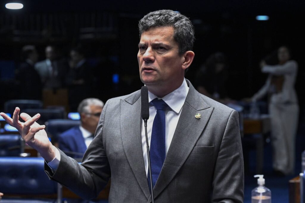 Por que os prefeitos do PL no Paraná estão considerando uma debandada? A filiação de Sergio Moro ao PL gerou insatisfação entre prefeitos do Paraná, que veem a mudança como uma quebra de acordos políticos anteriores. Qual foi a reação imediata dos prefeitos à filiação de Moro? Dezenas de prefeitos se reuniram em Curitiba, sinalizando apoio ao movimento de desfiliação liderado por Fernando Giacobo. Quem é Fernando Giacobo e qual seu papel nessa situação? Fernando Giacobo é deputado federal e ex-presidente do PL no Paraná. Ele lidera a dissidência contra a filiação de Moro ao partido. Quais cidades têm prefeitos envolvidos na possível debandada? Prefeitos de cidades como Cascavel, Araucária e Pato Branco estão entre os que consideram deixar o PL. Qual é a posição de Marcel Micheletto sobre a situação? Marcel Micheletto, presidente da AMP, deixou o PL e defende a continuidade do apoio ao governo estadual. Por que Giacobo critica a filiação de Moro ao PL? Giacobo alega que a filiação de Moro quebra um acordo político anterior, além de criticar o histórico de Moro com Bolsonaro. Como o novo presidente do PL no Paraná pretende lidar com a situação? Filipe Barros, novo presidente do PL paranaense, planeja abrir diálogo com prefeitos e parlamentares do partido. Qual é a situação do PL no cenário político do Paraná após as eleições de 2024? O PL se tornou uma das legendas com mais prefeitos no Paraná, atrás apenas do PSD e PP. Para quais partidos os prefeitos dissidentes podem migrar? Os prefeitos dissidentes podem migrar para o PSD ou partidos aliados ao governador Ratinho Junior. Qual é a situação do PSD em relação às eleições de 2026? O PSD ainda não definiu seu candidato para as eleições de 2026, com nomes como Guto Silva e Alexandre Curi sendo cogitados. Quem é o candidato da oposição ao governo do Paraná? Requião Filho, do PDT, será o candidato da oposição, em aliança com o PT. Como a filiação de Moro ao PL pode impactar a política estadual? A filiação de Moro pode causar uma reconfiguração das alianças políticas no Paraná, afetando o equilíbrio de poder local. Qual é a importância do apoio do governador Ratinho Junior nesse cenário? O apoio do governador é crucial para definir alianças e candidatos, influenciando diretamente o cenário político estadual. Quais são os desafios enfrentados pelo PSD na escolha de seu candidato? O PSD enfrenta dificuldades em encontrar um candidato com forte apoio e desempenho nas pesquisas eleitorais. Como a situação atual pode afetar as eleições de 2026 no Paraná? A debandada de prefeitos e a indefinição de candidatos podem alterar significativamente o cenário eleitoral de 2026 no estado.
