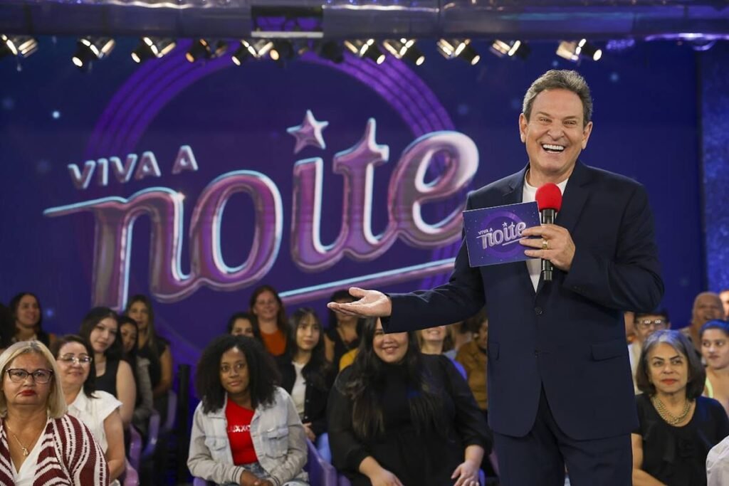 O que é o "Viva a Noite" e por que está voltando ao SBT? "Viva a Noite" é um clássico da TV que retorna ao SBT em uma versão repaginada, misturando nostalgia e modernidade. Comandado por Luis Ricardo, o programa busca resgatar a essência que conquistou o público nas décadas de 1980 e 1990. Quem são os apresentadores e convidados do programa? Luis Ricardo lidera o show, acompanhado por Liminha e Rafinha Viscardi. A estreia traz artistas como Maurício Gasperini, Ovelha, Fábio Villa, Renata Banhara, Cida Marques e Katia Romão, além da cantora internacional Nicki French. Quais quadros clássicos e novidades o programa apresenta? O programa resgata quadros icônicos como "Prova da Bexiga" e introduz novidades como "Que desenho é esse?" e "Artista Disfarçado", onde um convidado se disfarça de Elvis Presley, desafiando os participantes a descobrirem sua identidade. Como o "Viva a Noite" conecta gerações diferentes? Combinando o clima vintage com uma linguagem atual, o programa atrai tanto o público nostálgico quanto a nova geração, apresentando artistas do passado e desafios modernos, como o "Tarzan Brasileiro", que promete divertir todas as idades. Quando e onde assistir à estreia do "Viva a Noite"? A estreia da primeira temporada de "Viva a Noite" acontece neste sábado, às 22h30, no SBT. O programa promete ser um revival emocionante de um dos formatos mais icônicos da televisão brasileira. 📺