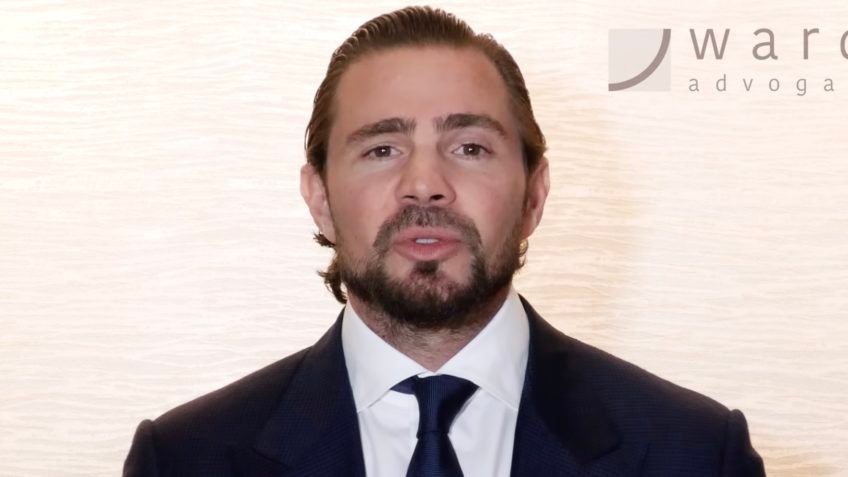 Uma frase dita com aparente tranquilidade pode ganhar outro peso quando o tempo passa e novas peças entram no tabuleiro. Que frase foi essa? A de que o acesso ao Judiciário brasileiro seria “muito bem formatado”. A declaração foi feita por Daniel Vorcaro, fundador do Banco Master, em junho de 2024, num vídeo gravado para a série Grandes Temas, Grandes Nomes do Direito, da TV Conjur. À primeira vista, parecia apenas mais uma fala institucional sobre o funcionamento das instituições. Mas por que essa fala voltou a chamar atenção agora? Porque ela não veio isolada. Vorcaro falava sobre a Suprema Corte, defendia que o Judiciário existe para proteger as leis e a Constituição e dizia que há mecanismos fortes de controle em todas as esferas. Também afirmou que o país tem juízes de qualidade e que isso gera estabilidade para o sistema judiciário brasileiro. Tudo isso soaria protocolar, então onde está o ponto que muda a leitura? Ele aparece quando se observa o ambiente em que essa declaração foi feita. O vídeo foi publicado no YouTube em 21 de junho de 2024, mas havia sido gravado durante uma viagem a Londres. E é justamente aí que muita gente começa a prestar mais atenção. O que havia de especial nessa viagem? Na capital britânica acontecia o Fórum Jurídico Brasil de Ideias, realizado de 24 a 26 de abril de 2024 e patrocinado pelo Banco Master. O evento reuniu juízes de cortes superiores, e Vorcaro chegou a comentar em mensagens com a então namorada, a modelo Martha Graeff, que havia discursado diante de ministros do STF e do STJ. Mas há um detalhe que quase passa despercebido: o vídeo em que ele elogia o acesso ao Judiciário foi gravado nesse mesmo contexto. Isso por si só explica tudo? Não exatamente. Só que acrescenta uma camada importante. O conteúdo da TV Conjur teve patrocínio do escritório de advocacia de Walfrido Warde, cujo logotipo aparecia ao fundo da gravação. Esse escritório, segundo as informações disponíveis, foi contratado por Vorcaro por um período. Então a questão deixa de ser apenas o que foi dito e passa a incluir onde, quando e em qual ambiente institucional a fala surgiu. E o que mais ele disse naquele vídeo? Além do elogio ao Judiciário, Vorcaro também exaltou o Banco Central. Afirmou que o sistema financeiro brasileiro é muito avançado, inclusive em comparação com países desenvolvidos, e disse que a autoridade monetária brasileira é reconhecida como uma das mais avançadas do mundo. Parece uma defesa ampla das engrenagens do Estado. Mas por que isso ganha outra dimensão depois? Porque os fatos posteriores ampliaram o interesse sobre suas relações institucionais. O nome de Vorcaro passou a aparecer em investigações sobre fraudes contra o sistema financeiro. Ele firmou em 19 de março um acordo de confidencialidade com a Polícia Federal e com a Procuradoria-Geral da República, etapa inicial para uma delação premiada. Está preso na Superintendência da PF em Brasília. E é aqui que a maioria se surpreende: uma fala antes vista como institucional passou a ser relida à luz de conexões, encontros e contratos que vieram a público depois. Mas o que, exatamente, havia naquele evento de Londres além dos discursos? Houve também uma degustação de whisky Macallan no George Club, em Mayfair, com custo de US$ 640.831,88, cerca de R$ 3,2 milhões no câmbio da época, segundo documentos encaminhados pela PF à CPMI do INSS. Cerca de 40 pessoas participaram, entre elas autoridades como Alexandre de Moraes e o diretor-geral da PF, Andrei Rodrigues. Ao final, os convidados receberam uma garrafa de Macallan como presente. O que acontece depois disso muda a forma como aquele cenário é observado. Por quê? Porque a viagem, o fórum, o vídeo, as mensagens e os desdobramentos judiciais passaram a compor um mesmo mosaico. Não se trata de inventar sentidos ocultos, mas de notar que a frase sobre um acesso ao Judiciário “bem formatado” foi dita num momento em que Vorcaro circulava em ambientes de alta influência, diante de ministros e autoridades, com o banco patrocinando parte relevante daquele contexto. Então qual é o ponto principal? Que a declaração de 2024 não virou notícia apenas pelo conteúdo, mas pelo contraste entre o tom de confiança institucional e tudo o que se revelou depois sobre a posição de Vorcaro, seus vínculos e o alcance de suas relações. A frase continua a mesma. O que mudou foi o peso de cada palavra quando colocada ao lado do restante da história. E talvez seja justamente isso que ainda deixe a pergunta em aberto: quando alguém diz que o sistema é “bem formatado”, está descrevendo uma estrutura sólida ou revelando, sem perceber, o tipo de proximidade que poucos conseguem alcançar?