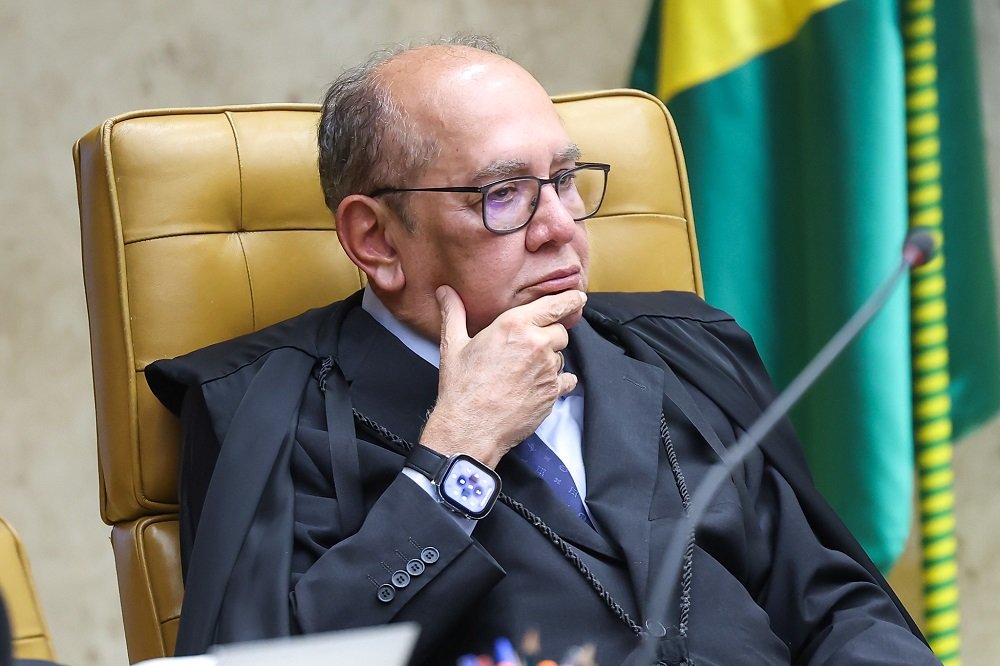 Quando um ministro do Supremo chama um pedido de indiciamento de “cortina de fumaça”, a pergunta não é só sobre o ataque, mas sobre o que ele diz estar sendo escondido. Por que essa reação chamou tanta atenção? Porque não se tratava de uma crítica genérica, nem de uma divergência discreta entre instituições. O alvo da vez era um ministro da mais alta Corte do país, incluído num relatório que pedia seu indiciamento por crimes de responsabilidade. E, ao responder, ele não apenas rejeitou a acusação como tentou inverter o foco: em vez de discutir o conteúdo do pedido, apontou para o que considerou um desvio de finalidade. Mas o que exatamente ele contestou? Segundo a manifestação publicada nesta terça-feira, a crítica central foi jurídica e política ao mesmo tempo. De um lado, ele afirmou que indiciamento é ato privativo de delegado de polícia e que isso não se aplica a crimes de responsabilidade. De outro, sustentou que esse tipo de rito cabe à Mesa do Senado, à Comissão Especial e ao Plenário da Casa, sem previsão de atuação de CPI nesse ponto. Se é assim, por que o relatório avançou nessa direção? É aí que a discussão ganha outra camada. O documento foi apresentado no encerramento de uma comissão voltada ao crime organizado e não se limitou a mapear facções, milícias ou medidas de segurança pública. Ele também pediu o indiciamento de integrantes do STF e do procurador-geral da República. E é justamente aqui que muita gente trava: como uma CPI criada para investigar um tema tão específico termina mirando ministros da Suprema Corte? A resposta está no próprio relatório final, que ultrapassa 200 páginas e mistura diagnósticos sobre o avanço de facções com acusações contra autoridades. No caso de um ministro, o texto fala em decisões sob suspeição e possível conflito de interesses. Em outro, aponta atuação em processos em que poderia haver impedimento. E, no caso de quem reagiu publicamente, menciona conduta incompatível com o decoro por anular medidas e determinar a inutilização de dados considerados relevantes para investigações. Mas há um ponto que quase passa despercebido: a resposta não ficou restrita à defesa pessoal. O que ele fez, então? Tentou deslocar o debate para a própria atuação da CPI. Disse que a comissão, instalada após a operação policial que vitimou mais de 120 pessoas nos Complexos do Alemão e da Penha, no Rio de Janeiro, não promoveu sequer a quebra de sigilos de milicianos ou líderes de facções criminosas. E essa observação muda o peso da fala, porque sugere que o problema, para ele, não é apenas ser citado no relatório, mas ver a comissão abandonar o foco que justificou sua criação. Mas por que isso importa tanto? Porque, ao dizer que o relatório tenta criminalizar decisões judiciais, o ministro não está apenas negando as acusações. Ele está afirmando que houve uma tentativa de transformar divergências sobre atos do Judiciário em matéria penal ou política sem base legal. E aqui surge a dúvida que mantém o caso aceso: trata-se de fiscalização legítima ou de constrangimento institucional? Na visão dele, a resposta é clara. As CPIs são instrumentos legítimos de controle do poder, mas perdem credibilidade quando usadas de forma panfletária ou como mecanismo de pressão entre instituições. Mais do que isso, ele afirmou que esse uso pode até configurar abuso de autoridade. Só que o que acontece depois complica ainda mais o cenário: o relatório não atinge apenas um nome. Quem mais aparece no pedido? Além dele, o documento pede o indiciamento dos ministros Dias Toffoli e Alexandre de Moraes, além do procurador-geral Paulo Gonet. No caso de Gonet, a CPI aponta omissão diante de indícios contra autoridades. Isso amplia o alcance político do texto e ajuda a explicar por que a reação foi tão dura. Não era uma crítica isolada, mas uma ofensiva com potencial de tensionar ainda mais a relação entre Senado, STF e Ministério Público. E quem assina esse movimento? O relator da CPI do Crime Organizado, senador Alessandro Vieira, apresentou o texto no último dia de atividades da comissão, que seria encerrada após não ser prorrogada pelo presidente do Senado, Davi Alcolumbre. A votação do relatório estava prevista para a mesma tarde. No meio desse fechamento, ainda era aguardado o depoimento do ex-governador do Rio, Cláudio Castro, que informou que não compareceria por problemas de saúde. Parece detalhe lateral, mas não é: mostra como a reta final da CPI terminou cercada de tensão, ausências e mudança de foco. No fim, o ponto principal aparece com nitidez: Gilmar Mendes não tratou o pedido de indiciamento apenas como uma acusação contra seu nome, mas como uma tentativa de desviar a CPI do combate ao crime organizado para um ataque ao STF com objetivos eleitorais. Essa é a acusação mais forte de sua resposta. Só que ela não encerra a história. Pelo contrário. Ela abre uma pergunta ainda maior: quando uma CPI deixa de investigar o crime e passa a disputar poder, quem realmente está no centro do relatório?