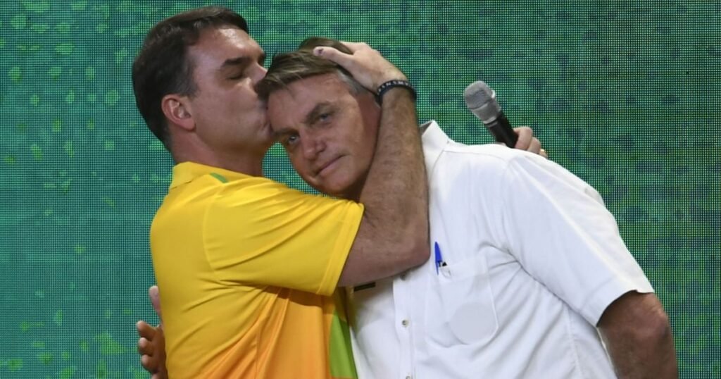 A declaração veio carregada de confronto: **“Bolsonaro foi julgado por inimigos”**. Quem disse isso e em que contexto? A fala foi do senador **Flávio Bolsonaro (PL-RJ)**, nesta segunda-feira (6), ao comentar a condenação do ex-presidente **Jair Bolsonaro (PL)**. Mas por que a afirmação ganhou repercussão imediata? Porque ela foi feita no momento em que Flávio, **pré-candidato à Presidência da República**, reagia à decisão que condenou seu pai a **27 anos e três meses de prisão** por **tentativa de golpe de Estado**. A crítica não ficou no campo genérico. O senador citou nominalmente ministros do **STF** e questionou a imparcialidade do julgamento. Quais foram exatamente as palavras usadas por Flávio? Em entrevista ao podcast **Inteligência Ltda.**, ele afirmou: **“Ele foi julgado por seus inimigos. Alexandre de Moraes é um inimigo declarado. Flávio Dino, antes de virar ministro, dizia que Bolsonaro era um demônio na Terra. Zanin era advogado do Lula até ontem. Está pagando um preço alto sem cometer crime nenhum”**. E a quem ele se referia ao falar em “inimigos”? Flávio mencionou diretamente os ministros **Alexandre de Moraes**, **Flávio Dino** e **Cristiano Zanin**. A declaração foi apresentada como uma contestação à composição do julgamento que resultou na condenação do ex-presidente. Quem condenou Jair Bolsonaro? A decisão foi tomada pela **Primeira Turma do STF**. Além do relator, **Alexandre de Moraes**, votaram pela condenação os ministros **Flávio Dino**, **Cármen Lúcia** e **Cristiano Zanin**. Houve divergência? Sim. O ministro **Luiz Fux** ficou vencido. Depois de votar pela **absolvição**, ele não participou da definição da pena. E qual é a situação de Bolsonaro após a condenação? O ex-presidente está em **prisão domiciliar humanitária**. Como isso foi definido? **Alexandre de Moraes** autorizou a medida por um período de **90 dias**, quando Bolsonaro foi internado no fim de março. O que justificou essa autorização? Segundo a decisão, a medida levou em conta os **problemas de saúde** do ex-presidente. Quais problemas? Bolsonaro enfrentou uma **broncopneumonia bilateral**, condição citada como base para a concessão da prisão domiciliar. Por que a fala de Flávio se concentra tanto nos ministros? Porque sua reação não tratou apenas da condenação em si, mas da legitimidade de quem participou dela. Ao citar nomes e históricos públicos, o senador procurou sustentar a acusação de que o pai não teria sido julgado por magistrados neutros, e sim por pessoas que, segundo ele, já tinham posição contrária ao ex-presidente. Essa crítica altera os fatos do julgamento? O que está registrado é que **Jair Bolsonaro foi condenado a 27 anos e três meses de prisão por tentativa de golpe de Estado**, por decisão da **Primeira Turma do STF**, com votos de **Alexandre de Moraes**, **Flávio Dino**, **Cármen Lúcia** e **Cristiano Zanin**, enquanto **Luiz Fux** votou pela absolvição e não participou da fixação da pena. Também está registrado que **Moraes** autorizou a **prisão domiciliar humanitária por 90 dias** após a internação de Bolsonaro no fim de março, com justificativa baseada em seus **problemas de saúde** e no quadro de **broncopneumonia bilateral**. E foi nesse cenário que Flávio Bolsonaro declarou, no **podcast Inteligência Ltda.**: **“Ele foi julgado por seus inimigos. Alexandre de Moraes é um inimigo declarado. Flávio Dino, antes de virar ministro, dizia que Bolsonaro era um demônio na Terra. Zanin era advogado do Lula até ontem. Está pagando um preço alto sem cometer crime nenhum.”**