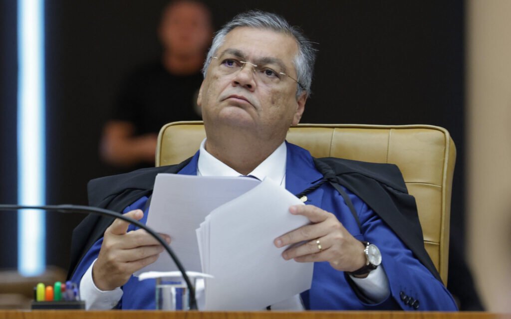 Quando ministros da mais alta Corte entram na mira de um pedido de indiciamento, a pergunta surge quase sozinha: o que está realmente em jogo? A resposta imediata parece simples, mas não é. Não se trata apenas de um embate político, nem de mais um capítulo de tensão entre instituições. O que apareceu foi uma reação pública, direta e calculada, de um integrante do próprio Supremo Tribunal Federal diante de um movimento que atingiu colegas de toga. E isso levanta outra dúvida: por que essa defesa ganhou tanto peso? Porque ela não veio de fora. Veio de dentro do tribunal. Flávio Dino publicou um texto em defesa de colegas do STF que foram incluídos no relatório final de uma CPI. Mas por que esses nomes foram parar ali? Essa é a parte que faz o caso sair do comum. O relatório final da CPI do Crime Organizado, elaborado pelo senador Alessandro Vieira, pediu o indiciamento de três ministros do Supremo: Dias Toffoli, Alexandre de Moraes e Gilmar Mendes. Além deles, também foi citado o procurador-geral da República, Paulo Gonet. Só isso já seria suficiente para provocar reação. Mas há um ponto que quase passa despercebido: quando um relatório de CPI alcança integrantes do topo do Judiciário e da Procuradoria, o impacto deixa de ser apenas jurídico e passa a ser institucional. E por que Dino decidiu se manifestar? Porque, ao defender os colegas, ele não estava apenas comentando um episódio isolado. Ele estava respondendo a um gesto que atinge diretamente a imagem, a autoridade e o funcionamento de instituições centrais da República. E é aqui que muita gente se surpreende: a discussão não gira só em torno dos nomes citados, mas do significado de colocá-los formalmente sob suspeita em um documento político. Mas o que exatamente Dino fez? Segundo a informação disponível, ele publicou um texto em defesa dos colegas de tribunal incluídos no relatório. Isso, por si só, já muda o tom do episódio. Em vez de silêncio ou distância, houve posicionamento. E quando um ministro escolhe falar, a pergunta seguinte se impõe: ele estava apenas protegendo aliados ou sinalizando algo maior? A resposta, com base no que foi divulgado, aponta para uma defesa institucional. Ainda assim, isso abre outra camada de curiosidade. Se a CPI avançou a esse ponto, o que motivou o relator a pedir o indiciamento de figuras tão centrais? O dado confirmado é que o pedido partiu de Alessandro Vieira, relator da CPI do Crime Organizado. O restante, sem extrapolar os fatos disponíveis, permanece no terreno da disputa política e jurídica que agora tende a se intensificar. Só que existe um detalhe que quase ninguém percebe à primeira leitura: o centro da notícia não está apenas no pedido feito pela CPI, mas na reação que ele provocou dentro do Supremo. Isso porque pedidos assim podem até gerar manchetes imediatas, mas o que acontece depois costuma definir o verdadeiro peso do episódio. E o que vem depois, neste caso, muda tudo. Por quê? Porque quando um ministro do STF sai em defesa pública de outros ministros atingidos por um relatório parlamentar, o caso deixa de ser apenas uma acusação formal em papel. Ele passa a ser também uma disputa de narrativa, de legitimidade e de autoridade entre esferas de poder. E isso reabre a pergunta inicial sob outra luz: estamos diante de um fato isolado ou de mais um sinal de atrito entre instituições? A resposta ainda não está fechada. O que já se sabe é que Flávio Dino se posicionou para defender Dias Toffoli, Alexandre de Moraes e Gilmar Mendes, além de reagir ao alcance do relatório que também incluiu Paulo Gonet. O pedido de indiciamento foi feito no relatório final da CPI do Crime Organizado, sob relatoria de Alessandro Vieira. Esse é o núcleo do caso. Mas o ponto principal aparece justamente no fim: mais do que defender nomes específicos, Dino entrou em campo para contestar o avanço de uma CPI sobre figuras centrais do Judiciário e da Procuradoria. E quando isso acontece, a notícia deixa de ser apenas sobre quem foi citado. Ela passa a ser sobre até onde uma crise institucional pode ir — e sobre o que ainda pode surgir a partir dessa reação.