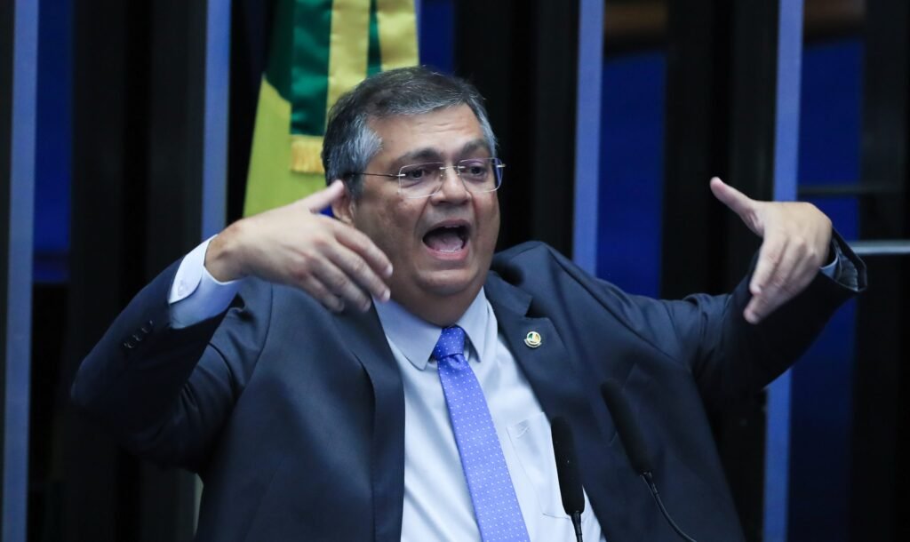 Chamar uma instituição de “o maior problema nacional” pode parecer só uma frase forte, mas, desta vez, a reação foi ainda mais explosiva. Por quê? Porque a resposta não veio em tom burocrático, nem escondida em nota técnica, mas com uma expressão pesada, calculada e impossível de ignorar: “gigantesco erro histórico”. Quando alguém escolhe palavras assim, a pergunta surge sozinha: o que exatamente estava sendo rebatido? A resposta começa em uma publicação feita nesta terça-feira, 14. Nela, o ministro Flávio Dino afirmou que apontar o Supremo Tribunal Federal como “o maior problema nacional” é um erro grave. Mas por que ele decidiu se manifestar justamente agora? Porque o ambiente já estava tensionado por um movimento político que elevou o conflito de patamar. Mais cedo, a Comissão Parlamentar de Inquérito do Crime Organizado divulgou trechos de seu relatório final. E é aqui que muita gente se surpreende: o documento não ficou restrito a criminosos, facções ou redes ilegais. Então quem entrou na mira? Segundo o relatório, ministros do STF e também o procurador-geral da República passaram a ser alvo de indiciamento. Isso muda o peso da discussão, porque deixa de ser apenas uma crítica institucional e passa a atingir diretamente nomes do topo do sistema de Justiça. Mas há um ponto que quase passa despercebido: Dino, ao reagir, não citou nomes. Por que isso importa? Porque, mesmo sem mencionar diretamente os envolvidos, ele deixou claro o alvo da crítica ao sustentar que o STF e a PGR têm um “relevante conjunto de decisões judiciais contra o crime organizado no Brasil”. Em outras palavras, a defesa não foi pessoal no sentido explícito, mas institucional no conteúdo. E isso abre outra dúvida: se ele fala em combate ao crime, o que estaria sendo ignorado no debate? Segundo o próprio ministro, ignorar a atuação dessas instituições e transferir a elas a responsabilidade pelos problemas nacionais é um equívoco. Só que ele foi além. O que vem depois altera o foco da discussão: Dino classificou como irresponsável investigar o crime organizado sem incluir milícias, traficantes, vendedores de armas ilegais, garimpos ilegais, facções que controlam territórios, além de matadores e pistoleiros. E por que essa lista chama tanta atenção? Porque ela desloca o centro da narrativa. Em vez de aceitar que o principal problema esteja no tribunal, ele sugere que o país corre o risco de inverter prioridades. Mas isso encerra o assunto? Longe disso. Se a fala foi uma defesa institucional, houve também um gesto político? A própria mensagem indica que sim, ainda que de forma contida. Dino afirmou que sua condição de magistrado o impede de comentar amplamente o tema, mas registrou solidariedade pessoal aos colegas alvo de injustiças. Essa combinação entre limite formal e recado direto é o tipo de detalhe que mantém a tensão no ar. Mas afinal, quem foram os ministros citados no relatório da CPI? O relator da comissão, senador Alessandro Vieira, indiciou Gilmar Mendes, Alexandre de Moraes e Dias Toffoli. E é aqui que a maioria volta a prender a atenção, porque o relatório não ficou apenas na crítica política: ele atribuiu aos três crimes de responsabilidade, o que, em tese, poderia embasar pedidos de impeachment. Com base em quê? Vieira argumentou que Moraes e Toffoli teriam agido de modo incompatível com a honra, a dignidade e o decoro de suas funções por causa da relação mantida com o Banco Master. Já em relação a Gilmar Mendes, o senador apontou a suspensão de quebras de sigilo da CPI, dizendo que isso teria servido para proteger os colegas. Então o que Flávio Dino realmente quis marcar com sua fala? No centro de tudo, a mensagem foi esta: transformar o STF no “maior problema nacional” distorce o debate sobre o crime organizado e, na visão dele, desvia a atenção de ameaças concretas que atuam com violência, dinheiro ilegal e controle territorial. Esse é o ponto principal. Mas o que acontece depois pode mudar ainda mais o peso dessa disputa, porque quando uma CPI avança sobre ministros do Supremo e a reação vem com a acusação de “erro histórico”, o embate deixa de ser apenas sobre investigação e passa a ser também sobre quem está definindo, afinal, onde está o verdadeiro problema do país.