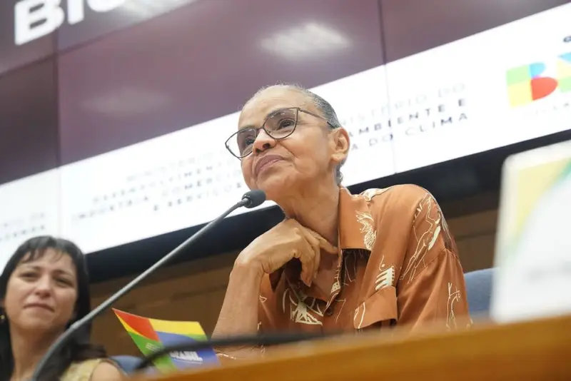 A permanência de **Marina Silva** na **Rede** provocou uma reação dura e pública da direção nacional do partido. Mas por que a decisão de continuar na própria legenda gerou tanta tensão? Porque a escolha veio em meio a um conflito já exposto entre a ex-ministra e a cúpula partidária, aprofundado por uma troca de notas oficiais que tornou o racha ainda mais visível. O que exatamente disse a direção da sigla? Em nota assinada no domingo (5) e divulgada na terça-feira (7), a direção nacional afirmou estar **perplexa** e **indignada** com a decisão de Marina de permanecer no partido. A legenda também declarou que jamais sugeriu sua saída, mesmo diante de divergências políticas anteriores, como o apoio à candidatura presidencial de **Aécio Neves** em 2014, ao **impeachment de Dilma Rousseff** e à **intervenção federal no Rio de Janeiro** em 2018. Se o partido diz que nunca pediu sua saída, então onde está o centro do conflito? A resposta aparece na acusação de falta de diálogo e no embate sobre o funcionamento interno da legenda. A direção afirma que Marina se recusa a dialogar com a cúpula e rebate críticas sobre autoritarismo. Segundo a nota, **“não atender pretensões pessoais de uma liderança não é autoritarismo. É compromisso com a vida democrática interna”**. O texto ainda sustenta que a democracia exige respeito às decisões coletivas e não o direito de uma minoria de paralisar o partido, judicializar impasses políticos ou tentar bloquear suas contas. E o que Marina Silva respondeu diante disso? Ao anunciar que não mudaria de partido, ela afirmou que pretende trabalhar na **“restauração dos princípios e valores da Rede”**. Para sustentar sua posição, recorreu ao **manifesto de fundação** da legenda. Também declarou a intenção de fortalecer alianças com o **PSOL**, com quem a Rede compõe uma federação, e com outros cinco partidos: **PT**, **PSB**, **PV**, **PDT** e **PCdoB**. Marina classificou essas siglas como legendas que não se deixam capturar pelo **autoritarismo** e pelo **negacionismo**. A reação à manifestação dela ficou restrita à direção nacional? Não. Na mesma postagem, o coordenador de comunicação da Rede, **Marco Mills Martins**, chamou a manifestação de **“desrespeitosa”** e **“repleta de inverdades”**. Ele também acusou a cúpula de não ter submetido a nota à aprovação dos membros e pediu que fosse apurado o **uso indevido das redes do partido** para essa finalidade. Esse embate é apenas político ou também chegou à Justiça? Chegou à Justiça. A divisão interna tem, do outro lado, a deputada federal **Heloísa Helena**. Ela e Marina travam uma batalha judicial pela presidência do partido, em uma ação que inclui acusações de irregularidades em congressos internos. A direção da Rede afirma que Marina pratica **lawfare**, expressão usada para se referir ao uso do Judiciário como campo de batalha política. E o que a legenda diz sobre as decisões judiciais? A nota sustenta que, ao contrário do que se tenta fazer crer, a Justiça **não anulou o 5º Congresso Nacional da Rede**. Segundo a direção, a maior parte das ações foi rejeitada e a atual direção segue plenamente reconhecida, inclusive com integrantes do grupo de Marina em sua composição. Diante de tanta disputa, qual foi o recado final da direção nacional? A legenda afirmou que todos os que quiserem se filiar são bem-vindos, desde que respeitem **as regras partidárias** e **o bom convívio**. E, sobre os palanques de **2026**, declarou que as decisões serão tomadas no âmbito do partido, com **diálogo**, **bom senso**, de forma **altiva** e **sem interferências externas**.