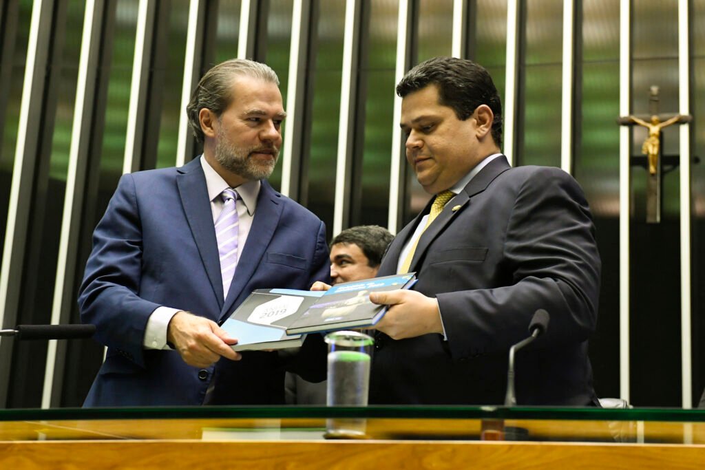 Não é só uma disputa política, e é justamente isso que torna tudo mais explosivo. Quando alguém afirma que a direita poderá fazer o impeachment dos “imorais” e acabar com a “máfia do sistema”, a primeira pergunta surge quase sozinha: isso é apenas retórica de campanha ou a acusação aponta para algo maior? A resposta, segundo o conteúdo apresentado, é que se trata de algo maior. A tese central é que existe uma blindagem entre setores do Planalto, do Judiciário e do Congresso, formando uma rede de proteção mútua que impediria investigações, travaria punições e manteria intocados personagens poderosos. Mas se essa blindagem existe, por que ela seria tão difícil de romper? Porque, de acordo com o texto, o problema não estaria isolado em um único órgão. A denúncia fala em infiltração em várias esferas de poder, com efeitos sobre decisões judiciais, investigações sensíveis e escândalos bilionários. E então aparece uma dúvida ainda mais incômoda: o que estaria sendo protegido com tanta força? A resposta aponta para casos que, segundo a descrição, envolvem o roubo bilionário dos aposentados do INSS, o escândalo de R$ 80 bilhões do Banco Master e a possibilidade de uma delação seletiva. Ou seja, a preocupação não seria apenas com corrupção em tese, mas com a preservação de nomes influentes. Só que há um detalhe que quase ninguém percebe: o texto não trata isso como um problema do passado, e sim como uma engrenagem ainda funcionando. Se a engrenagem continua ativa, quem seriam os alvos principais da crítica? A resposta vem com peso: ministros do STF, lideranças petistas, presidentes da Câmara e do Senado e o banqueiro Daniel Vorcaro aparecem ligados, no argumento do artigo, por relações que levantariam suspeitas de favorecimento, amizade imprópria, proteção institucional e conflito de interesses. Mas por que a cobrança recai com tanta força sobre ministros da Suprema Corte? Porque o texto sustenta que ministros não podem ignorar ética, julgar em causa própria, agir politicamente ou manter vínculos que comprometam a imparcialidade. E é aqui que muita gente se surpreende: a crítica não fica no campo abstrato da moralidade. Ela menciona o princípio da suspeição dos juízes, presente no Direito Romano, no Código Civil e no Código de Ética da Magistratura, para dizer que certas condutas seriam incompatíveis com o cargo. Mas quais condutas estariam no centro dessa acusação? A descrição cita, entre outros pontos, a atuação de Dias Toffoli no caso Master, a menção a negócios no resort Tayayá, a história de Flávio Dino com precatórios e sigilo bancário, e, de forma ainda mais contundente, as ligações atribuídas a Alexandre de Moraes com Daniel Vorcaro. O que acontece depois muda o tamanho da denúncia: o texto afirma que a Polícia Federal teria usado código-fonte para confirmar pedido de Vorcaro ao ministro para evitar a liquidação do banco. Se isso é tão grave, por que nada teria avançado? A resposta apresentada é política. Segundo o artigo, pedidos de impeachment estariam sendo segurados porque o comando institucional permanece nas mãos de grupos interessados em manter a proteção recíproca. E aqui surge a virada que reativa a curiosidade: se o sistema se protege por dentro, qual seria a única forma de quebrar esse ciclo? A resposta do texto é direta: eleição. Mais especificamente, a vitória de candidatos da direita em 2026. Sem mudar o comando político, diz a argumentação, seria muito difícil investigar, punir e desmontar essa estrutura. Mas isso significaria apenas trocar nomes ou alterar o equilíbrio de poder? Pelo que se sustenta no artigo, seria alterar o equilíbrio de poder. A ideia é que só uma nova maioria política poderia destravar investigações, enfrentar ministros acusados de abuso e corrupção, e levar adiante processos hoje paralisados. Só que existe um ponto ainda mais delicado: por que o tema é tratado como algo que afeta diretamente o cidadão comum? Porque, segundo a descrição, o custo dessa blindagem não fica restrito aos bastidores de Brasília. Ele recai sobre cofres públicos, aposentadorias, poupança, confiança nas instituições e futuro do país. A “máfia do sistema”, nessa narrativa, não seria uma metáfora vazia, mas um mecanismo que drena recursos e protege poderosos enquanto a população paga a conta. E qual é, afinal, o ponto principal? Que o impeachment de ministros do STF e o enfrentamento dessa rede de proteção, na visão do texto, dependem menos de denúncias isoladas e mais de uma mudança política profunda em 2026. O desfecho prometido não estaria nos tribunais de agora, mas nas urnas que ainda virão. E é justamente aí que a história, em vez de terminar, começa a ficar mais perigosa.