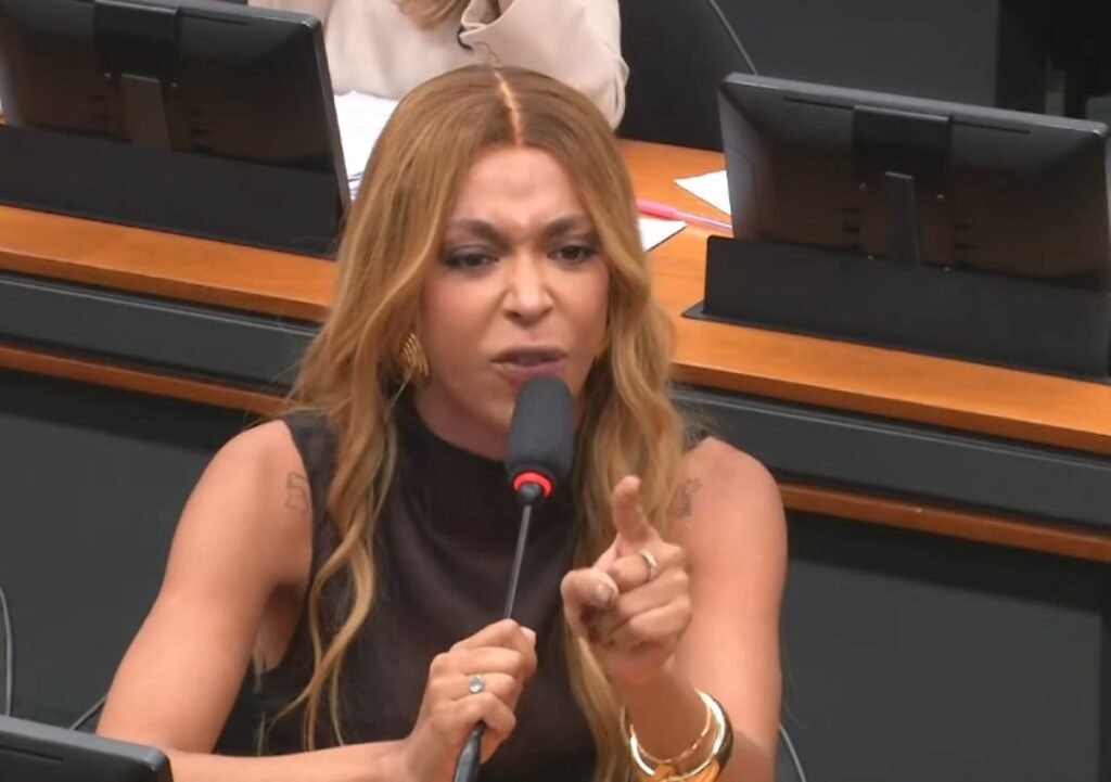 Bastou uma frase para transformar a sessão em confronto aberto. O que parecia ser apenas mais uma reunião da **Comissão de Defesa dos Direitos da Mulher**, realizada na **Câmara dos Deputados**, em Brasília, acabou mergulhando em um clima de tensão que rapidamente saiu do controle. Mas o que levou a esse ponto? Tudo começou quando entrou em pauta uma **moção de repúdio** contra a presidenta do colegiado, a deputada federal **Erika Hilton**, do **PSOL de São Paulo**. A sessão ocorreu na quarta-feira, **8 de abril**, e foi marcada por discussões fortes, trocas de acusações e um ambiente cada vez mais carregado. Ainda assim, a pergunta que ficou no ar foi outra: por que a reação dela chamou tanta atenção? A resposta veio no momento em que deputadas usaram o microfone para afirmar: “**deputada Erika, Vossa Excelência não nos representa**”. Foi então que Erika rebateu de forma direta: “**Graças a Deus eu não as represento**”. A declaração elevou ainda mais a temperatura da sessão. Mas há um detalhe que quase ninguém percebe de imediato: essa resposta não veio isolada, e sim acompanhada de um desabafo mais amplo sobre sua presença naquele espaço. O que ela disse em seguida? Erika afirmou que, depois de toda a sua trajetória de vida, chegar até ali para representar mulheres com esse tipo de agenda seria o fim, e que preferia pegar suas coisas e sair dali. A fala expôs não apenas o desgaste do momento, mas também o tamanho do embate político instalado dentro da comissão. E é aqui que muita gente se surpreende: a deputada não limitou sua reação ao episódio daquela sessão. Ela também denunciou que sua eleição à presidência da comissão teria provocado um fenômeno que classificou como inédito. Que fenômeno foi esse? Segundo Erika, mulheres que nunca haviam pisado na **Comissão de Defesa dos Direitos da Mulher** passaram a aparecer ali pela primeira vez após sua entrada na presidência. Para ela, isso não aconteceu por interesse no trabalho do colegiado, mas para “**lacrar**” e usar o ódio contra sua figura como forma de gerar conteúdo para seus eleitores por meio da tática do **pânico moral**. E por que essa acusação ganhou tanto peso? Porque Erika afirmou ter observado o perfil dessas deputadas e o alcance que tinham antes do confronto. Segundo ela, eram **midiaticamente irrelevantes**, mas, ao irem à comissão fazer espetáculo e contraditar sua presidência, passaram a buscar números superiores aos que acumulavam de seguidores. O que acontece depois muda o rumo da discussão, porque a sessão deixou de girar apenas em torno da moção e passou a tocar em outro tema sensível. Qual foi esse tema? Em sua fala, Erika também criticou o modo como a **biologia** estaria sendo usada no debate. Ela declarou que, se houvesse real preocupação com a biologia, não se ignoraria que a biologia diz que não há vida até determinada semana de gestação, em referência ao **aborto**. E reforçou: “**E não sou eu que estou dizendo isso, não é a esquerda, não é a nossa opinião, quem diz isso é a biologia, é a ciência**”. Mas a sessão terminou ali? Não. A reunião foi marcada por **agressão verbal dentro da Casa** e acabou sendo **interrompida**. Esse desfecho consolidou o cenário de confronto que já vinha se formando ao longo da sessão e explicou por que o episódio repercutiu tanto. O centro da crise foi a entrada em pauta da **moção de repúdio contra Erika Hilton**, seguida pela reação da deputada às críticas, por suas acusações sobre o comportamento de outras parlamentares e por sua fala sobre **biologia**, **ciência** e **aborto**. No fim, foi isso que incendiou a comissão: uma sessão da **Comissão de Defesa dos Direitos da Mulher**, em **8 de abril**, na **Câmara dos Deputados**, marcada por tensão, discussões intensas, uma **moção de repúdio** contra **Erika Hilton**, a resposta “**Graças a Deus eu não as represento**”, a denúncia de uso de **pânico moral** e a interrupção da reunião após um episódio de **agressão verbal**.