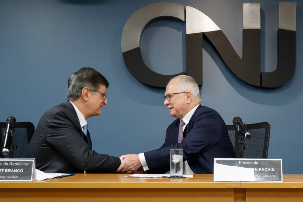 Bastaram **11 votos favoráveis** para destravar uma decisão que mexe diretamente com os ganhos de **juízes e procuradores**. Mas o que, de fato, está sendo aprovado? Trata-se de uma **resolução conjunta** do **CNJ** e do **CNMP** que consolida, enquanto não houver uma **lei nacional**, a negociação conduzida no **STF** sobre as chamadas **verbas indenizatórias** que ficam fora do **teto remuneratório do funcionalismo público**. Quem conduz esse voto que já formou maioria? O relator é o presidente do **CNJ** e do **STF**, ministro **Edson Fachin**. E em que ponto está a votação? A sessão virtual conjunta termina nesta sexta-feira, **9**, mas a maioria já foi alcançada, com **11 votos favoráveis**, restando **4** para a unanimidade. Mas o que essa resolução faz na prática? Ela define quais valores devem respeitar o teto e quais continuam fora dele. O que entra no limite? Valores pagos a título de **décimo terceiro**, **terço de férias**, **gratificação por acúmulo de funções eleitorais** e **pró-labore** não podem exceder o teto. E o que fica de fora? A proposta lista um conjunto de **penduricalhos** que escapam dessa regra. Quais são esses benefícios mantidos? Mesmo após críticas do ministro **Flávio Dino** a rubricas inusitadas, como **“auxílio-peru”** e **“auxílio iPhone”**, os tradicionais **auxílio-moradia** e **auxílio-saúde** foram preservados. Também permanecem fora do teto os gastos com **diárias** e uma **ajuda de custo para transferências**. Há novidade entre os benefícios? Sim. O texto cria a **gratificação de proteção à primeira infância e à maternidade**. Como ela funciona? **Juízes e procuradores** passarão a receber **3% do próprio salário para cada filho de até seis anos de idade**. Esse valor pode ser acumulado pelo casal? Não. Se dois servidores forem casados, o benefício não poderá ser acumulado. E existem outras formas de pagamento extra previstas? Sim. Uma delas tem descrição mais ampla e será concedida a quem atuar em **“comarca, sede, função, ofício ou unidade de difícil provimento”**. Além disso, **Judiciário** e **Ministério Público** continuarão podendo pagar valores adicionais a quem **não utilizar férias**, a quem **seguir trabalhando mesmo após cumprir os requisitos para aposentadoria** e a quem **acumular funções**. Esses penduricalhos terão um limite geral? Não exatamente. A limitação de **35% da remuneração** não foi aplicada de forma global. O que isso significa? Significa que algumas verbas foram submetidas a esse percentual de maneira separada, e não como um teto único para o conjunto dos benefícios. Como isso aparece no texto? As **gratificações por acumulação de cargos** e por atuação em locais de **difícil provimento**, por exemplo, não podem atingir, juntas, esse percentual. Ao mesmo tempo, a **indenização por valorização por tempo de antiguidade na carreira** também está, paralelamente, submetida a esse teto. Ou seja, a trava não foi estabelecida sobre todos os penduricalhos somados. Há alguma medida voltada à transparência? Sim. No fim, a proposta determina a padronização de dados em **portais de transparência**. O que deverá ser informado? **Nome dos benefícios** e **valores brutos e líquidos**. E, afinal, o que fica consolidado com a maioria já formada? Fica encaminhada a aprovação da resolução conjunta relatada por **Edson Fachin**, com **11 votos favoráveis**, para manter fora do teto remuneratório verbas como **auxílio-moradia**, **auxílio-saúde**, **diárias**, **ajuda de custo para transferências**, pagamentos por atuação em local de **difícil provimento**, valores por **acúmulo de funções**, por **não usufruir férias**, por **continuar em atividade após preencher requisitos para aposentadoria** e ainda a nova **gratificação de proteção à primeira infância e à maternidade**, de **3% do salário para cada filho de até seis anos**, sem acúmulo entre cônjuges servidores.