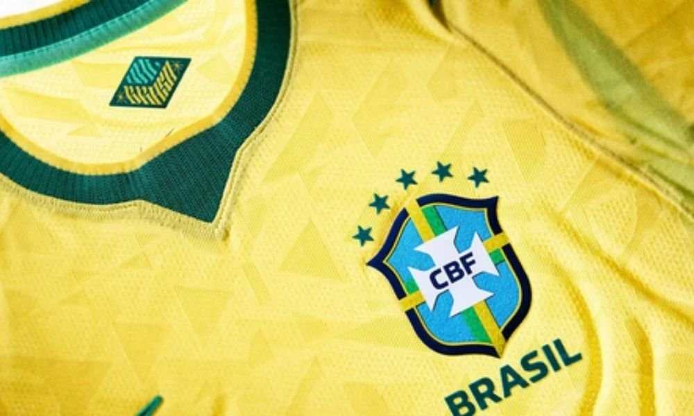 Algo aparentemente pequeno começou a chamar atenção justamente onde menos se esperava: no **ombro** de camisas feitas para o maior palco do futebol. Mas como um detalhe tão específico virou assunto a apenas **dois meses da Copa do Mundo**? Porque ele não apareceu em uma peça isolada, nem em um lote desconhecido. O problema foi percebido em **vários uniformes de seleções nacionais**, e isso muda completamente o peso da história. Que problema é esse, afinal? Segundo relatos divulgados pela imprensa britânica, o que ficou visível foi um **estufamento ao redor das costuras dos ombros**. Não se trata de uma falha de desempenho, pelo menos de acordo com a própria fabricante, mas de algo que compromete a **estética geral** da camisa. E quando o assunto é uniforme de seleção, aparência nunca é só aparência. Por que isso importa tanto se o desempenho não foi afetado? Porque a camisa de uma seleção não é apenas um item técnico. Ela é símbolo, identidade, imagem global e também produto de consumo em massa. E é justamente aí que a situação ganha outra dimensão: o problema não estaria apenas nas camisas usadas em campo, mas também nas **réplicas vendidas aos torcedores**. Então os jogadores e os fãs estariam vendo o mesmo defeito? De acordo com a **BBC**, sim. E isso ajuda a explicar por que alguns torcedores passaram a demonstrar preocupação. Afinal, se a falha aparece tanto no uniforme profissional quanto no modelo comercial, a dúvida deixa de ser pontual e passa a ser estrutural. Mas quais seleções foram afetadas? É aqui que muita gente começa a prestar ainda mais atenção. O estufamento foi visto em camisas de equipes como **Inglaterra**, **França** e **Uruguai**. E há um detalhe que quase ninguém percebe de imediato: essas não são seleções periféricas no torneio. São equipes de enorme visibilidade, o que amplia o impacto da falha. Isso significa que o problema pode ser ainda maior? A resposta mais prudente é: possivelmente, sim. A empresa produz uniformes para várias seleções da Copa, incluindo **Estados Unidos**, **Canadá**, **Brasil**, **Holanda** e **Croácia**. Não foi dito que todas foram afetadas, mas o simples alcance da fornecedora já basta para manter o alerta aceso. E por que esse defeito apareceu justamente agora? Porque os uniformes foram desenvolvidos com **tecnologia de resfriamento**, pensada para ajudar os jogadores a enfrentar as **altas temperaturas** esperadas no torneio, que começa em **11 de junho** e também será co-organizado pelo **México**. O que acontece depois muda tudo: quando uma peça é criada para unir inovação, conforto e imagem, qualquer falha visual passa a levantar dúvidas sobre o equilíbrio entre essas três promessas. A empresa reconheceu o problema? Sim, mas de forma contida. Um porta-voz disse ao jornal **The Guardian** que a Nike identificou um **“pequeno problema”** nos uniformes. Ao mesmo tempo, afirmou que o desempenho não foi comprometido, embora a **estética geral não esteja onde precisa estar**. Parece uma admissão simples, mas ela abre uma pergunta inevitável: se a estética não está no nível esperado, o que será feito a tempo? E é aqui que a maioria se surpreende: a questão surge num momento delicado para a empresa. A Nike já vinha enfrentando dúvidas sobre a **inovação de seus produtos** e também lidando com **excesso de estoque**, após uma sequência de **lucros fracos**. Ou seja, o problema das camisas aparece justamente quando a marca tenta reafirmar sua capacidade de liderar tecnicamente o mercado. Isso ajuda a explicar os movimentos recentes? Tudo indica que sim. O presidente-executivo **Elliott Hill** prometeu reorientar a Nike para os **esportes principais**, e a empresa anunciou a nomeação de **Andy Caine** como diretor de inovação. Coincidência ou resposta a um cenário mais amplo? A informação oficial não fecha essa conta por completo, mas deixa claro que o tema inovação está no centro da discussão. Então qual é o ponto principal dessa história? Não é apenas uma costura, nem apenas um incômodo visual. O que está em jogo é a imagem de uma marca global às vésperas de um torneio gigantesco, com um problema visível em camisas de seleções importantes, presente tanto no campo quanto nas lojas. A Nike está investigando, mas a dúvida que continua no ar é a mais incômoda de todas: se um **pequeno problema** já ficou tão visível agora, o que ainda pode aparecer quando os holofotes da Copa estiverem totalmente acesos?
