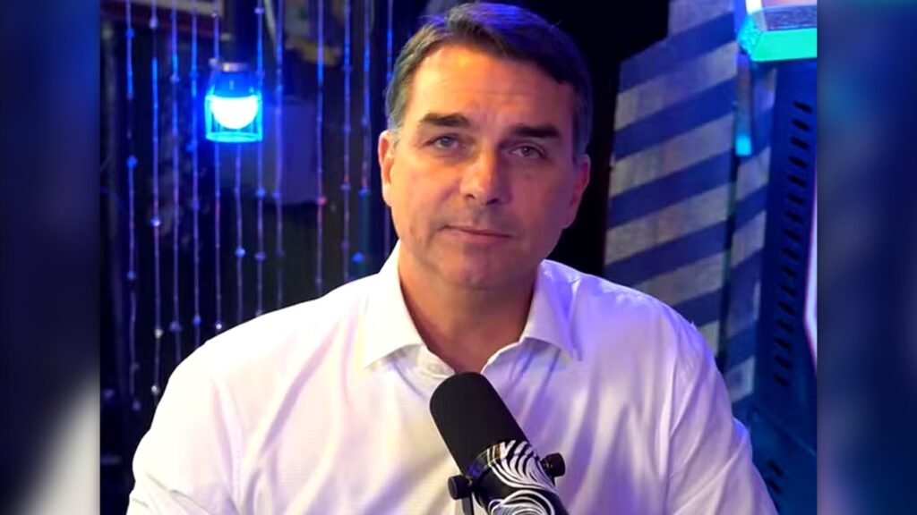Bastou o assunto voltar à mesa para reacender uma das acusações mais sensíveis da política recente. O que Flávio Bolsonaro disse agora sobre a **“rachadinha”**? Nesta segunda-feira, 6, o senador afirmou que pretende enfrentar esse tema durante a **pré-campanha presidencial** e voltou a negar qualquer envolvimento nas cobranças atribuídas ao ex-assessor **Fabrício Queiroz**. Mas por que essa declaração chama atenção neste momento? Porque ela retoma um caso que marcou sua trajetória pública e que, mesmo após decisões judiciais e o arquivamento da denúncia, continua sendo lembrado no debate político. Ao falar em entrevista ao podcast **Inteligência Ltda**, Flávio reconheceu que Queiroz admitiu ter cobrado parte dos salários de funcionários, mas afirmou que **não sabia** da prática. E como ele descreveu essa situação? Segundo o senador, Queiroz cuidava de uma parte de sua assessoria ligada à **panfletagem na rua**. Foi nesse contexto que, de acordo com Flávio, o ex-assessor teria dito que contratava pessoas e cobrava uma parte do salário delas, sem que ele tivesse conhecimento disso. Na entrevista, o senador declarou: “Toda essa espuma de tentar destruir minha reputação… nunca respondi criminalmente por isso. Queiroz cuidava de uma parte da minha assessoria que fazia panfletagem na rua. Ele falou que tinha pessoas que ele contratou e que cobrava uma parte do salário, e colocou no papel que eu jamais tinha conhecimento disso”. Mas de onde surgiu essa investigação? O caso começou em **2018**, a partir de relatórios do **Conselho de Controle de Atividades Financeiras**, o **Coaf**. Esses documentos apontaram movimentações consideradas **atípicas** no gabinete de Flávio Bolsonaro, que à época era **deputado estadual** na **Assembleia Legislativa do Rio de Janeiro**. E o que aconteceu a partir daí? O **Ministério Público do Rio de Janeiro** chegou a denunciá-lo por **peculato**, **lavagem de dinheiro** e **organização criminosa**. A acusação avançou com base em provas reunidas durante a investigação, o que colocou o caso no centro da atenção pública e política. Então por que a denúncia não seguiu adiante? Porque decisões do **STF** e do **STJ** anularam provas consideradas relevantes para o processo. Entre os elementos invalidados estavam **quebras de sigilo bancário** e **relatórios financeiros**. Sem essas provas, a base da acusação foi enfraquecida. E qual foi a consequência prática dessa invalidação? Em **2022**, o Ministério Público pediu o **arquivamento da denúncia**. A justificativa foi direta: os elementos que restaram após a anulação das provas não sustentavam a acusação. Isso significa que Flávio usa esse ponto para sustentar sua defesa? Sim. Ao voltar a falar sobre o caso, ele reforça que **nunca respondeu criminalmente** pela acusação e insiste que não tinha conhecimento das cobranças feitas por Queiroz. Ao mesmo tempo, sinaliza que não pretende evitar o tema durante a pré-campanha, mas sim enfrentá-lo publicamente. E o que fica, afinal, da fala mais recente? Fica a reafirmação de uma linha de defesa que ele mantém desde o avanço das investigações: **Fabrício Queiroz admitiu a cobrança de parte dos salários de funcionários, mas Flávio Bolsonaro diz que jamais teve conhecimento disso**. Também fica o histórico do caso: a investigação começou em **2018** com base em relatórios do **Coaf** sobre movimentações atípicas no gabinete, o **Ministério Público do Rio** o denunciou por **peculato**, **lavagem de dinheiro** e **organização criminosa**, e depois o **STF** e o **STJ** anularam provas relevantes, como **quebras de sigilo bancário** e **relatórios financeiros**. Com isso, em **2022**, o Ministério Público pediu o **arquivamento da denúncia**, alegando que os elementos remanescentes não sustentavam a acusação.