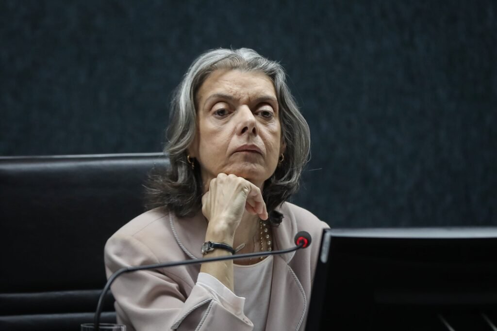 Quando uma ministra do **Supremo** diz em público que as pessoas podem “dormir tranquilas”, a pergunta surge sozinha: por que alguém sentiria necessidade de dizer isso agora? A resposta começa em um ambiente de **desconfiança**. Nos últimos tempos, o comportamento de integrantes do **STF** passou a ser observado com ainda mais intensidade, e isso ajuda a explicar o peso de uma frase como **“Eu não faço nada errado”**. Mas por que essa declaração chamou tanta atenção? Porque ela não veio isolada. Veio acompanhada do reconhecimento de que existe uma **tensão** real dentro da Corte. E quando uma ministra admite esse clima, a dúvida seguinte é inevitável: tensão provocada por quê? Segundo a própria fala, o tribunal vive um momento mais difícil em meio a uma crise de imagem e a um país marcado por **desconfiança generalizada**. Isso não significa apenas pressão externa. Significa também que cada gesto, cada agenda e cada aparição pública passam a ser lidos como sinais de algo maior. Mas há um ponto que quase ninguém nota de imediato: a ministra não falou em nome de todos. Ela fez questão de delimitar o terreno e defender a própria **lisura**. Disse que não há “uma linha” sua fora da lei. E é justamente aí que muita gente para por um segundo: se a defesa é tão pessoal, o que isso revela sobre o momento vivido pelo tribunal? Revela, no mínimo, que a cobrança por **transparência** se tornou central. Em vez de rejeitar esse escrutínio, ela afirmou que o **STF** precisa mostrar à população que está ali para servir. E isso leva a outra pergunta importante: como fazer isso de forma concreta? A resposta apareceu quando ela falou das agendas dos magistrados. Para Cármen Lúcia, é saudável que juízes saiam dos gabinetes para ouvir a sociedade. Mas isso, segundo ela, exige prestação de contas. É preciso saber **como sair, para onde ir e como tornar isso transparente**. E aqui está uma virada que prende a atenção: ela usou a própria rotina como exemplo. Ao afirmar que todos sabiam que ela estava naquele evento e que suas **agendas são públicas**, a ministra transformou um princípio abstrato em recado direto. Só que isso abre uma nova dúvida: por que reforçar tanto esse ponto justamente agora? A resposta passa pelo contexto de atenção pública em torno do **caso Banco Master** e também por relatos de **divisões internas** no tribunal. Mesmo sem detalhar esses episódios, a fala dela se encaixa nesse cenário de cobrança crescente. E o que acontece depois muda o foco da discussão: a tensão institucional também aparece no plano pessoal. Cármen Lúcia relatou que a vida no tribunal se tornou **“mais tensa e muito mais difícil”**. Disse ainda ser alvo constante de **críticas ácidas** e de discursos **sexistas, machistas e desmoralizantes**. Quando uma ministra expõe esse tipo de pressão, a pergunta deixa de ser apenas jurídica ou política. Ela passa a ser humana: até onde vai o custo de permanecer nesse lugar? A própria resposta impressiona. Segundo ela, familiares já sugeriram que deixasse a cadeira no **STF**. E é aqui que muitos se surpreendem, porque a reação da ministra não foi a de recuo. Nos momentos de pressão, ela diz repetir para si mesma: **“você faz direito, não milagres”**. A frase parece simples, mas carrega um sentido maior. Se não há milagres, então o que se espera de fato da Corte? Na visão dela, o tribunal enfrenta uma realidade interna marcada por **excesso de demandas** e por questões inéditas, muitas impulsionadas pelas **redes sociais**. Ela resumiu isso de forma direta: **cada manhã traz uma indagação nunca feita antes na história da humanidade**. Mas essa constatação resolve o problema ou apenas mostra o tamanho dele? Talvez mostre os dois. Porque, ao mesmo tempo em que reconhece a dificuldade, a ministra também faz uma defesa institucional de quem ocupa a chefia do tribunal. Disse saber o que é estar na presidência tentando acertar e afirmou que **não é simples**. O ponto principal, então, aparece no fim com mais força do que no começo: ao falar em tensão, transparência e ataques pessoais, Cármen Lúcia não tentou negar a crise — tentou marcar publicamente de que lado quer ser vista dentro dela. E essa diferença, num momento como este, diz mais do que parece.