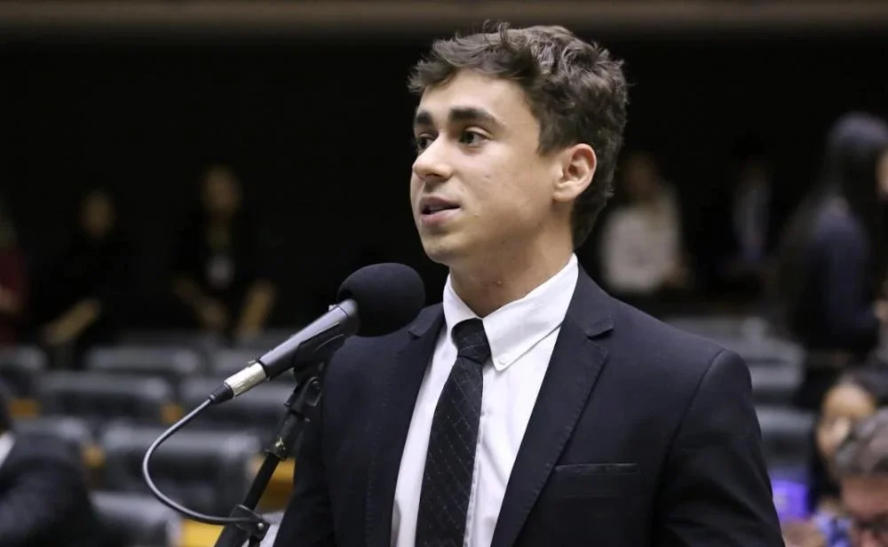 A reação veio com recado direto e expôs uma ferida na direita. O que aconteceu? Nikolas Ferreira respondeu a uma publicação de Flávio Bolsonaro que pedia união da direita nesta sexta-feira. E por que isso chamou atenção? Porque a resposta não foi apenas um gesto de apoio. Ela também trouxe um desabafo sobre ataques, divisões e cobranças dentro do próprio campo conservador. O que Flávio havia defendido? O senador e pré-candidato à Presidência pediu união da direita. A fala abriu espaço para uma resposta que misturou lealdade, incômodo e prioridade política. O que Nikolas disse primeiro? Ele afirmou que vem sofrendo provocações há três anos e que, até aqui, permaneceu calado. Mas por que ele resolveu falar agora? Porque, segundo o deputado, o problema deixou de atingi-lo sozinho. Ele disse que aliados antigos, leais e íntegros, também passaram a ser alvo da mesma turma. Que turma é essa? Nikolas não citou nomes. Mas afirmou que são pessoas que, em vez de somar, geram divisão e até fiscalização ou perseguição. Perseguição por quê? Segundo ele, por causa do nível de exposição nas redes. Na crítica feita por Nikolas, há cobrança até sobre quem não publica a porcentagem de conteúdo que esse grupo deseja. Isso chegou a que ponto? O deputado afirmou que até cor de camisa virou argumento para conflito. Esse detalhe muda o tom da fala? Muda porque mostra o grau de desgaste que ele quis denunciar. Não se trata apenas de divergência política. Na visão dele, o ambiente virou disputa por sinais, aparência e demonstrações públicas de fidelidade. E qual foi a resposta de Nikolas a esse tipo de cobrança? Ele fez uma distinção clara. Disse que postar alguém todos os dias é fácil. Difícil, segundo ele, é conquistar votos por meio das ideias que a pessoa representa. O que ele quis dizer com isso? Que apoio político, para ele, não se resume a repetição em rede social. Ele defendeu que o trabalho efetivo está em convencer, mobilizar e transformar ideias em voto. Essa fala foi uma defesa pessoal? Também. Ela responde diretamente a críticas sobre sua atuação e sua lealdade. Mas o texto parou no desabafo? Não. E é aí que está a virada. Depois de expor o desgaste, Nikolas declarou apoio explícito a Flávio Bolsonaro. O que ele prometeu? Disse que fará de tudo para que Flávio chegue ao Planalto. Essa foi a parte mais forte? Foi uma das mais claras. Mas ele foi além ao ligar esse apoio a outras bandeiras do campo bolsonarista. Quais? Nikolas afirmou que as pessoas do dia 8 merecem anistia. Também citou os perseguidos políticos. E incluiu Jair Bolsonaro nessa defesa. Como ele se referiu ao ex-presidente? Chamou Bolsonaro de o homem que mudou o país. Também disse que sempre demonstrou lealdade e gratidão a ele. Então a mensagem foi de unidade total? Foi de unidade, mas com um aviso embutido. Nikolas deixou claro que há um conflito interno desgastando a direita. Ainda assim, afirmou que permanecerá calado diante disso. Por quê? Porque, segundo ele, há um país para salvar. Essa frase resume o centro da mensagem? Resume. Ela mostra que, para o deputado, a disputa principal não está dentro da direita. Está fora dela. E como ele encerrou? Com uma frase que concentra o sentido político do texto. Nikolas disse que acredita em Flávio e pediu que Deus o ilumine para tomar as decisões certas. Depois veio o ponto principal. Qual? “Nosso inimigo é outro.” Por que essa frase pesa tanto? Porque ela tenta reorganizar o foco da direita. Em vez de alimentar brigas internas, a mensagem aponta para um adversário externo. No contexto político atual, isso funciona como chamado à disciplina e à convergência. O que fica dessa reação? Fica o retrato de uma direita pressionada por disputas internas, mas ainda tentando se alinhar. Fica também a defesa de que lealdade não se mede só por postagem. E, perto do fim, fica a revelação central. Apesar das provocações que disse sofrer há anos, Nikolas escolheu reafirmar apoio a Flávio Bolsonaro. Com uma condição implícita. Parar de gastar energia com divisão. Porque, na leitura dele, o alvo real está em outro lugar.