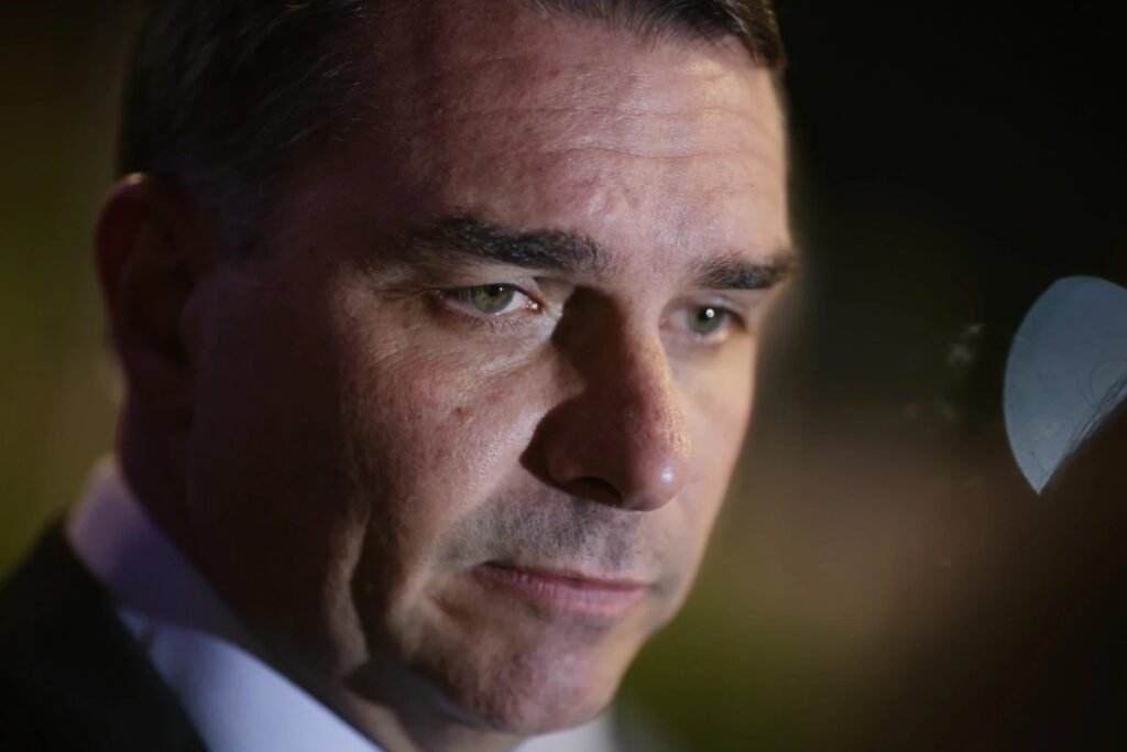 Uma investigação pode, sozinha, mudar o destino de uma candidatura presidencial? A pergunta parece exagerada à primeira vista, mas é justamente esse tipo de movimento que acende o alerta quando o assunto envolve **direitos políticos**, **elegibilidade** e o peso de uma eventual **condenação**. Mas por que esse caso chamou tanta atenção agora? Porque não se trata apenas de uma disputa jurídica comum. O que entrou no radar foi a possibilidade de um nome já colocado como **pré-candidato ao Planalto** enfrentar um obstáculo que vai muito além do desgaste político. Se houver condenação, o efeito pode atingir o ponto mais sensível de qualquer projeto eleitoral: a capacidade de disputar a eleição. E qual seria exatamente esse efeito? Segundo o advogado especializado em direito eleitoral **Carlos Frota**, uma eventual condenação pode levar à **suspensão dos direitos políticos**. E é aqui que muita gente se surpreende: quando isso acontece, o problema não é apenas “ficar mal na foto” ou perder apoio. O impacto é objetivo. Sem direitos políticos em pleno exercício, o cidadão deixa de preencher requisitos básicos para entrar na corrida eleitoral. Mas isso significa inelegibilidade automática? O ponto levantado pelo especialista é que, em caso de condenação, a **Constituição Federal de 1988** prevê a suspensão dos direitos políticos. Frota foi direto ao afirmar que, sem entrar no caso concreto, a sentença penal condenatória, inclusive por **crimes contra a honra**, pode produzir esse efeito. E se os direitos políticos forem suspensos, surge uma consequência prática que muda tudo. Que consequência é essa? A impossibilidade de obter a **certidão de quitação eleitoral**. Pode parecer um detalhe técnico, mas está longe de ser algo secundário. Sem essa certidão, a pessoa não é sequer registrável. Em outras palavras, não consegue formalizar candidatura. E há um detalhe que quase ninguém percebe: o bloqueio não para aí. O que mais muda? De acordo com o advogado, com a suspensão dos direitos políticos o cidadão também **não pode se filiar a partido político**, **não pode votar** e ainda tem o **título eleitoral cancelado**. Ou seja, não se trata apenas de uma barreira para concorrer. É uma interrupção ampla da participação política formal. E isso ajuda a explicar por que o caso passou a ser visto como algo com potencial de colocar “o dedo na balança”. Mas de onde surgiu essa discussão? Ela ganhou força após a abertura de um **inquérito** determinada pelo ministro **Alexandre de Moraes**, do **STF**, para investigar um possível **crime de calúnia** contra o presidente **Lula**. A apuração mira uma postagem feita nas redes sociais em **3 de janeiro de 2026**. A decisão foi tomada a partir de representação da **Polícia Federal**, requerida pelo **Ministério da Justiça e Segurança Pública**. Isso quer dizer que a condenação já está no horizonte? Não. E esse ponto é essencial. O que existe, neste momento, é a abertura de investigação, com envio dos autos à **PF**, que terá **60 dias** para realizar as diligências iniciais. Ainda assim, o simples fato de o caso envolver um possível crime contra a honra já foi suficiente para levantar a discussão sobre os efeitos de uma eventual sentença condenatória. E é justamente essa possibilidade, ainda que futura, que mantém o tema em alta. Como foi a reação do senador? **Flávio Bolsonaro** afirmou ter recebido a decisão com “**profunda estranheza**” e disse que a medida seria “**juridicamente frágil**”, sustentando que a publicação investigada não teria tipicidade penal. A resposta política veio também de **Eduardo Bolsonaro**, que acusou Moraes de tentar influenciar uma eventual candidatura presidencial do senador. Mas por que essa reação ampliou ainda mais o debate? Porque o caso deixou de ser apenas uma discussão sobre uma postagem e passou a tocar em algo maior: a disputa sobre quem pode ou não chegar à urna. Quando entra em cena a hipótese de suspensão de direitos políticos, o debate jurídico rapidamente se mistura ao cálculo eleitoral. E o que acontece depois pode redefinir todo o cenário. No fim, o ponto central é simples e ao mesmo tempo explosivo: se houver **condenação**, Flávio Bolsonaro pode, sim, ficar impedido de disputar a Presidência, segundo a avaliação do especialista em direito eleitoral. Só que a história ainda está longe de terminar — porque, antes de qualquer desfecho, o que está em jogo não é apenas um inquérito, mas o impacto que ele pode ter no equilíbrio da próxima corrida pelo poder.