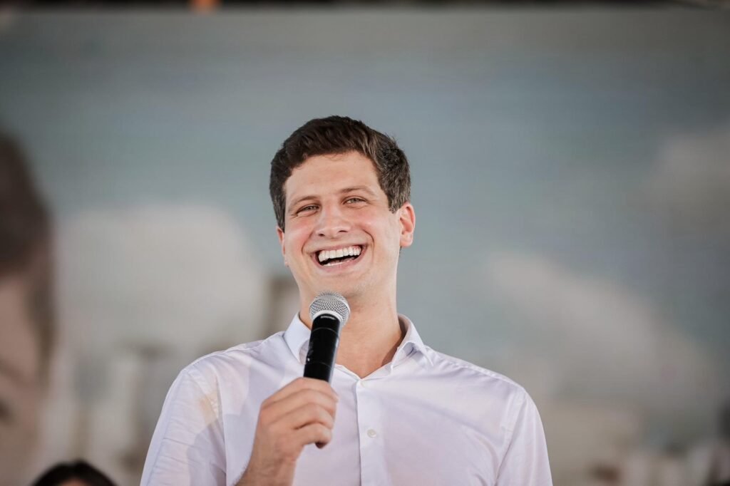 Uma placa pode transformar uma homenagem pública em suspeita de promoção política? Pode, e é exatamente isso que está no centro de uma denúncia que agora pede apuração formal. A questão não começou com uma obra inteira, nem com um discurso, nem com uma campanha aberta. Começou com um símbolo. E quando um símbolo aparece em um espaço que deveria servir ao interesse coletivo, a dúvida surge quase automaticamente: aquilo representa o poder público ou representa um partido? Mas por que isso virou caso de tribunal? Porque a denúncia foi protocolada no Tribunal de Contas do Estado de Pernambuco com um argumento direto: pode ter havido violação ao princípio da impessoalidade. Em outras palavras, o que se questiona é se um equipamento público recém-inaugurado teria sido usado de forma incompatível com o que a Constituição exige da administração pública. E é aqui que muita gente para e pensa: um simples detalhe visual seria suficiente para levantar uma acusação desse tamanho? Segundo o documento apresentado, sim. O ponto central é a presença de um símbolo partidário em uma placa instalada em um memorial público. Isso muda o peso da discussão, porque deixa de ser apenas uma crítica política e passa a ser uma suspeita de uso indevido da identidade de um partido dentro de uma estrutura estatal. Mas há um detalhe que quase passa despercebido: não se trata apenas da imagem em si, e sim do que ela pode significar quando colocada em um bem público. E qual seria esse símbolo? A denúncia afirma que a placa exibe a pomba com ramo de oliveira, símbolo que identifica o Partido Socialista Brasileiro. A legenda é presidida nacionalmente por João Campos. A partir daí, a acusação sustenta que o uso dessa identidade visual em espaço público pode ferir a Constituição, especialmente o artigo 37, que impõe impessoalidade, moralidade e legalidade à administração pública. Só que isso abre outra pergunta inevitável: onde exatamente esse símbolo teria sido colocado? Foi em um memorial dentro de um parque público. O espaço em questão é o Memorial Eduardo Campos, localizado no parque de mesmo nome. E é nesse ponto que o caso ganha uma camada ainda mais sensível. O memorial homenageia Eduardo Campos, pai de João Campos. A obra foi conduzida e entregue pela gestão do então prefeito. O que acontece depois muda o tom de toda a discussão: João Campos deixou recentemente a Prefeitura do Recife para disputar o governo estadual. Por que esse contexto pesa tanto? Porque, na avaliação do autor da denúncia, ele reforça a suspeita de uso político da estrutura pública. O vereador Thiago Medina, do PL, afirma que houve possível mistura entre interesse público e promoção política. Para ele, há indícios de desvio de finalidade e até de improbidade administrativa. Isso significa que a crítica não está restrita ao campo simbólico. Ela tenta enquadrar o caso como algo com possível consequência jurídica e administrativa. E é aqui que a maioria se surpreende: o pedido não ficou só na reclamação. O que foi solicitado? Medina pediu a retirada imediata do símbolo, a responsabilização dos envolvidos, a abertura de fiscalização pelo TCE-PE, a identificação dos responsáveis e o envio do caso ao Ministério Público. A frase usada por ele resume o argumento: espaço público não pode ser utilizado para promover partido político. A denúncia, portanto, não discute apenas gosto, estética ou interpretação. Ela questiona se houve violação objetiva de um princípio constitucional. Mas isso significa que já existe condenação ou decisão tomada? Não. Até o momento, o que existe é a denúncia formal e a expectativa de análise pelo tribunal. O TCE-PE pode pedir esclarecimentos, abrir diligências e até adotar medidas cautelares para garantir o uso correto de bens públicos. Ou seja, o caso ainda está na fase em que os fatos serão examinados. E há outro ponto importante: João Campos ainda não se manifestou sobre a acusação. Então qual é o ponto principal de tudo isso? É que a denúncia tenta transformar um elemento aparentemente discreto em prova de algo maior: o possível uso político de um espaço público. O centro da controvérsia não é apenas uma placa, mas o limite entre homenagem institucional e identificação partidária. E quando esse limite entra em disputa, a pergunta deixa de ser apenas o que foi colocado ali. A pergunta passa a ser por que foi colocado — e quem, de fato, se beneficiaria disso.