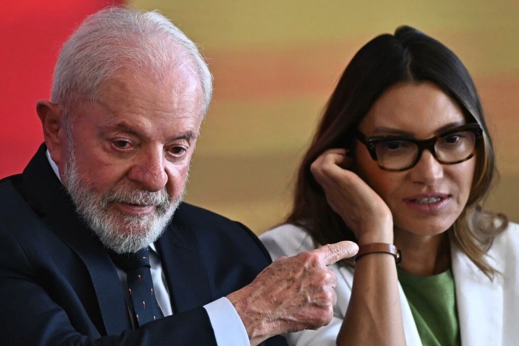 Uma correção feita em segundos mudou o peso inteiro de uma fala presidencial — e quase ninguém percebeu por que aquele detalhe importava tanto. O que foi dito de tão sensível assim? Durante um discurso sobre violência contra a mulher, uma palavra usada de forma ampla acabou sendo interrompida no meio do caminho. A frase parecia seguir normalmente, mas houve uma intervenção imediata, curta e direta, que obrigou uma reformulação ali mesmo, diante de todos. Mas por que uma única palavra geraria esse tipo de reação? Porque, quando o tema é violência doméstica e agressão contra mulheres, a forma como se nomeia o agressor altera o foco da mensagem. Dizer “pessoas” soa genérico. Dizer “homens” aponta para um recorte que, naquele contexto, a primeira-dama considerou essencial destacar. E quem fez essa interrupção? Foi Janja, Rosângela da Silva, que interpelou o presidente no momento em que ele mencionava prisões ligadas à violência contra a mulher. A correção veio no instante em que ele afirmava que a Polícia Federal havia prendido quase cinco mil “pessoas”. Janja sugeriu a troca do termo. Lula, então, refez a frase e passou a dizer “cinco mil homens”. Mas isso aconteceu em qualquer evento? Não. O episódio ocorreu em uma cerimônia no Palácio do Planalto, justamente durante a sanção da tipificação do crime de vicaricídio. E é aqui que muita gente se surpreende: o centro do evento já era, por si só, extremamente grave, porque tratava de um tipo de violência voltado a atingir uma mulher por meio do ataque à vida de pais, filhos ou dependentes. Então a correção foi apenas simbólica? Não exatamente. Ela aconteceu dentro de um discurso que buscava dimensionar a gravidade da violência. Depois de ajustar a frase, Lula reforçou a ideia de recorrência ao dizer que isso acontece “todo dia, toda hora” e que “90% a gente não sabe”. O que vem depois dessa fala muda a leitura do episódio, porque a discussão deixa de ser apenas sobre linguagem e passa a tocar na dimensão do problema. De onde vieram esses números citados no discurso? Segundo o próprio governo federal, as Operações Mulher Segura e Alerta Lilás resultaram na prisão de 5.238 pessoas entre 9 de fevereiro e 5 de março de 2026. Os dados foram divulgados em 6 de março e integram o Pacto Nacional de Enfrentamento ao Feminicídio. Mas há um detalhe que quase ninguém nota quando vê só o recorte da interrupção: os dados oficiais mencionam “pessoas”, não exclusivamente “homens”. E por que isso importa? Porque, embora a maior parte do debate público sobre violência contra a mulher esteja associada à agressão masculina, a própria legislação brasileira admite situações em que mulheres também podem ser enquadradas. Como assim? A Lei Maria da Penha prevê punições em casos de violência praticada por outras mulheres, desde que exista relação doméstica, familiar ou afetiva. Isso inclui, por exemplo, situações envolvendo casais homoafetivos, mãe e filha ou irmãs. Ou seja, juridicamente, o ponto central não é apenas o gênero da agressora, mas o vínculo e o contexto da violência. Então Janja estava errada ao pedir a mudança? A questão não aparece como um simples certo ou errado. O que o episódio expôs foi uma disputa de ênfase: de um lado, o dado oficial mais amplo, que fala em “pessoas”; de outro, a tentativa de marcar politicamente quem, em regra, aparece como principal autor desse tipo de crime. E é justamente nessa tensão que o momento ganha força. Por que isso repercutiu tanto? Porque não foi apenas uma correção técnica nem apenas uma cena de bastidor. Foi um instante público em que linguagem, política, estatística e simbolismo se cruzaram ao vivo. A fala foi corrigida no ato, sem cerimônia, e isso transformou um trecho de discurso em notícia. E o ponto principal, afinal, qual foi? Não foi só a “chamada” de Janja, nem apenas a resposta imediata de Lula. O núcleo da cena está no contraste entre a precisão política da mensagem e a precisão literal dos dados. Quando uma palavra muda, muda também o alvo da atenção. E, nesse caso, a troca revelou mais do que um ajuste de frase: revelou como o debate sobre violência doméstica também passa pela batalha para definir exatamente quem está sendo nomeado — e quem ainda fica fora dessa moldura.