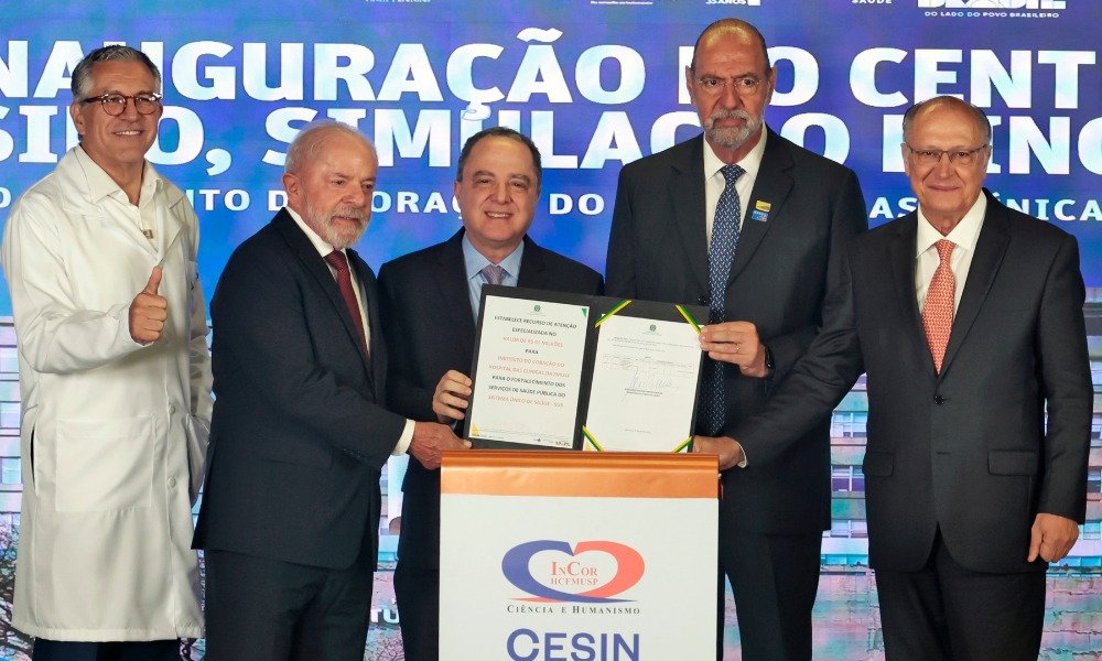 Uma assinatura pode parecer apenas mais um ato oficial. Mas, desta vez, ela mexe com uma das maiores urgências da saúde: o avanço de regras para desenvolver **vacinas contra o câncer** e ampliar o acesso a **medicamentos de alto custo**. O que exatamente foi decidido? Foi sancionada uma lei que cria um **marco regulatório** para orientar o desenvolvimento, a pesquisa, a produção, a distribuição e o acesso a essas vacinas no país. E por que isso chama tanta atenção? Porque o texto não fala só de ciência em laboratório. Ele conecta **inovação científica**, **produção nacional**, **colaboração internacional** e **acesso universal no SUS**. Mas isso significa que uma vacina contra o câncer já está pronta? Não. O ponto central não é anunciar uma cura imediata, e sim estabelecer as **normas** para que esse desenvolvimento aconteça com base regulatória definida. E é justamente aí que muita gente se surpreende: antes de qualquer avanço chegar ao paciente, existe um caminho de pesquisa, produção e acesso que precisa estar organizado. Então por que essa lei ganhou tanto peso? Porque ela também inclui **remédios de alto custo contra o câncer**, ampliando o alcance do marco regulatório. Em vez de tratar o tema de forma isolada, a nova lei reúne diretrizes para fomentar pesquisa, fortalecer a produção no país e buscar mais equidade no atendimento. Mas há um detalhe que quase ninguém percebe: quando se fala em acesso universal, o centro da discussão deixa de ser apenas a tecnologia e passa a ser também quem consegue, de fato, receber tratamento. E quem foi responsável por essa sanção? Foi o presidente **Lula**, nesta sexta-feira, dia 10, em **São Paulo**, durante um evento que não tratava apenas da nova lei. Isso muda alguma coisa? Muda porque o anúncio aconteceu ao lado da inauguração de uma estrutura voltada à formação, simulação e inovação em saúde, o que reforça o discurso de modernização do sistema público. Que estrutura é essa? Trata-se do **Centro de Ensino, Simulação e Inovação**, o **Cesin**, do **InCor** do Hospital das Clínicas da Faculdade de Medicina da USP. E por que isso importa dentro dessa notícia? Porque o ambiente inaugurado foi apresentado como uma peça estratégica para qualificar profissionais, reduzir riscos assistenciais e acelerar a incorporação de soluções inovadoras na prática clínica. Mas o que existe nesse centro para gerar tanta expectativa? O complexo tem **cinco andares**, **oito salas de simulação** com cenários como **emergência**, **UTI** e **centro cirúrgico**, além de **realidade virtual imersiva**, **biobanco** para armazenamento de material genético, área de inovação e espaços de ensino. O que acontece depois muda tudo: esse tipo de estrutura não serve apenas para treinar, mas também para testar e validar **novos dispositivos**, **terapias**, **processos assistenciais**, **tecnologias digitais** e até recursos de **inteligência artificial**. E quem participou desse momento? Além de Lula, estiveram presentes o ministro da Saúde, **Alexandre Padilha**, o ministro **Guilherme Boulos**, a primeira-dama **Janja Silva** e o vice-presidente **Geraldo Alckmin**. Mas a presença dessas autoridades foi só simbólica? Não exatamente. Padilha anunciou um pacote de **R$ 100 milhões** em investimentos no InCor, sendo cerca de **R$ 45 milhões** destinados à construção, implantação e equipamentos do novo centro. Só isso já explica a dimensão do evento? Ainda não. No mesmo dia, também foi formalizada a adesão do InCor como instituição mentora do projeto **Mais Médicos Especialistas** e assinado um repasse para implantação do **Núcleo de Telessaúde** do HCFMUSP, com investimento de mais de **R$ 9 milhões**. E por que isso entra na mesma narrativa? Porque a ideia apresentada foi expandir formação, especialização e atendimento para além de um único hospital, alcançando profissionais e pacientes de diferentes regiões do país. Mas existe algo ainda maior por trás desse conjunto de anúncios? Sim. O Ministério da Saúde informou a intenção de instalar no Hospital das Clínicas de São Paulo o primeiro **hospital público inteligente**, com **700 leitos**, uso de **inteligência artificial**, ambulâncias conectadas em **5G** e **telessaúde**. A promessa é reduzir o tempo de atendimento em casos graves de até **17 horas** para **2 horas**. Então qual é o ponto principal de tudo isso? No fim, a notícia não é apenas que **Lula sancionou uma lei**. É que o governo vinculou essa sanção a uma estratégia mais ampla: criar regras para desenvolver **vacinas contra o câncer**, incluir **medicamentos de alto custo**, reforçar a **produção nacional**, ampliar a **pesquisa** e sustentar a promessa de **acesso pelo SUS**. E esse é justamente o trecho que deixa a pergunta mais importante no ar: com a lei criada, como e quando essa estrutura vai se transformar em resultado concreto para quem mais precisa?