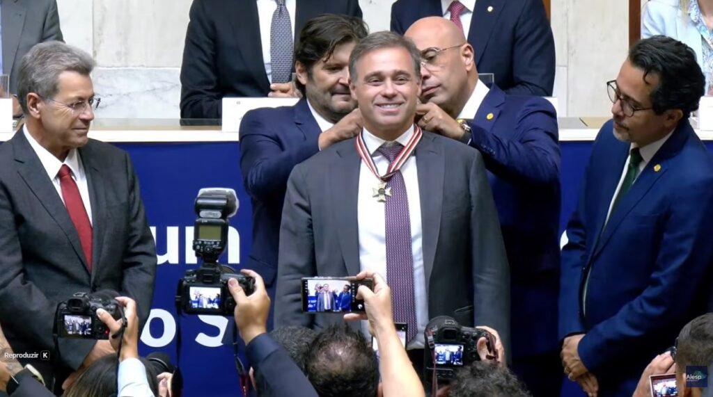 Uma homenagem reuniu, na mesma noite, nomes centrais da política e da Justiça em São Paulo — mas o que exatamente aconteceu na **Alesp**? Na noite de segunda-feira, dia **6**, o ministro do **Supremo Tribunal Federal**, **André Mendonça**, recebeu o **Colar de Honra ao Mérito** durante uma sessão solene realizada no plenário **Juscelino Kubitschek** da **Assembleia Legislativa de São Paulo**, na Zona Sul da capital. A cerimônia começou por volta das **20h30**, na **Avenida Pedro Álvares Cabral**, e foi conduzida pelo presidente da Alesp, o deputado estadual **André do Prado**. Mas por que essa homenagem chamou tanta atenção? Porque o evento reuniu autoridades de peso dos **Três Poderes** no estado e contou com a presença do governador **Tarcísio de Freitas**, do prefeito de São Paulo **Ricardo Nunes** e do presidente do **Tribunal de Justiça de São Paulo**, o desembargador **Francisco Eduardo Loureiro**. Também participaram deputados estaduais e federais convidados, entre eles **Cezinha de Madureira** e **Oseias de Madureira**. E quem propôs a homenagem? A outorga foi proposta pelo deputado estadual e pastor evangélico **Oseias de Madureira**. A solenidade também foi marcada por **apresentações religiosas**, compondo o ambiente da cerimônia em que o ministro recebeu a honraria sob aplausos e posou para fotos ao lado do governador e do prefeito. Mas o que representa o **Colar de Honra ao Mérito**? Trata-se de uma das principais honrarias concedidas pelo **Legislativo paulista**. Segundo a própria Casa, o reconhecimento é destinado a personalidades que prestaram **serviços relevantes ao estado**. Foi nesse contexto que autoridades destacaram a trajetória pública de André Mendonça ao longo da solenidade. E quais passagens dessa trajetória foram lembradas? Durante o evento, foram citadas suas atuações como **advogado-geral da União**, **ministro da Justiça** e integrante do **STF** desde **2021**. André Mendonça chegou ao Supremo em **dezembro de 2021**, indicado pelo ex-presidente **Jair Bolsonaro** para a vaga de **Marco Aurélio Mello**. O que o próprio ministro disse ao receber a homenagem? Em seu discurso, Mendonça agradeceu a presença dos convidados e associou a homenagem a um compromisso público. “**Obrigado por dedicarem o tempo precioso de vocês comigo. É um motivo de muita honra e de muita alegria. Vocês nos presenteiam com tudo isso. Diante dessa cerimônia, que devo agradecer, sinto a responsabilidade de comprometer, me responsabilizar com essa generosidade, fazer alguns compromissos públicos para que de fato eu faça jus a essas homenagens**”, afirmou. E por que seu nome segue em evidência além da cerimônia? Porque André Mendonça ocupa hoje posições de destaque no cenário institucional. O ministro é o novo relator do **caso Master** e já estava à frente da investigação no STF que apura **fraudes no INSS**. Além disso, será **vice-presidente do Tribunal Superior Eleitoral**, em composição com **Nunes Marques**, que comandará a Justiça Eleitoral. Como sua chegada ao STF aconteceu? Antes de assumir a cadeira no Supremo, Mendonça comandou a **AGU** e o **Ministério da Justiça**. Sua indicação foi feita por Bolsonaro, que havia declarado em discursos que escolheria para a Corte um ministro “**terrivelmente evangélico**”. A sabatina no Senado, porém, foi marcada por demora: segundo as informações publicadas, o então presidente da **CCJ**, senador **Davi Alcolumbre**, atrasou em cinco meses o processo do agora ministro. E qual foi, afinal, a cena que marcou a noite? Foi a entrega do **Colar de Honra ao Mérito** a **André Mendonça**, em sessão solene no plenário **Juscelino Kubitschek** da **Alesp**, com a presença de **Tarcísio de Freitas**, **Ricardo Nunes**, autoridades dos **Três Poderes**, aplausos, apresentações religiosas e o reconhecimento formal de uma das mais importantes honrarias do **Legislativo paulista**.