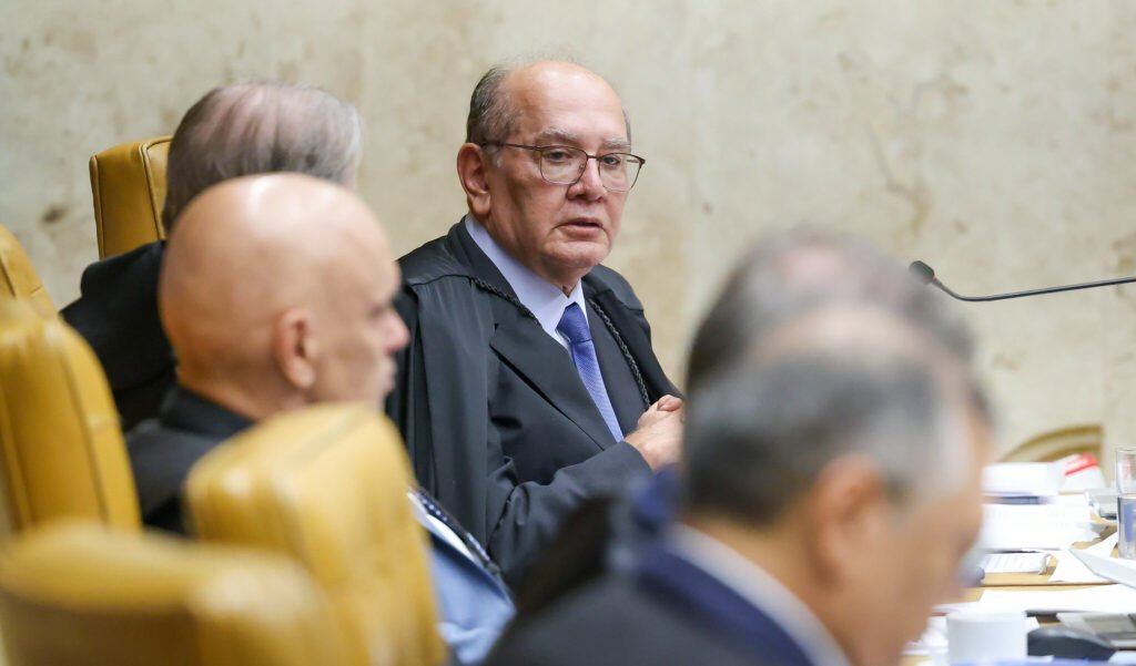 Uma frase dita no **Supremo** reacendeu uma ferida que o país acompanha há anos — e, ao mesmo tempo, lançou uma acusação direta sobre o que teria faltado quando mais se cobrava resposta. Mas o que foi dito de tão forte? Segundo **Gilmar Mendes**, houve um período em que a investigação de um dos crimes mais emblemáticos da política brasileira simplesmente não recebeu a **prioridade** que deveria. E essa crítica não foi genérica, nem abstrata. Ela teve alvo, momento e consequência. Qual foi o ponto central da fala? O ministro afirmou que o caso só avançou de fato depois da chegada de **Flávio Dino** ao **Ministério da Justiça**. Antes disso, na visão dele, a condução não teve o impulso necessário. E é justamente aí que surge a pergunta que prende tudo: se o avanço veio depois, o que teria faltado antes? A resposta apareceu em tom duro. Gilmar declarou que **Sergio Moro**, quando passou pelo ministério no governo **Jair Bolsonaro**, **“não colocou prioridade na investigação do caso Marielle”**. A frase ganhou ainda mais peso porque veio acompanhada de uma observação cortante: as razões, disse ele, “**o diabo Deus deve saber**”. Mas por que essa declaração chama tanta atenção agora? Porque ela não trata apenas de opinião política. Ela mexe com a narrativa sobre quem agiu, quem deixou de agir e em que momento a apuração começou a produzir resultados mais concretos. E há um detalhe que quase ninguém percebe de imediato: a fala foi feita durante uma sessão do STF sobre outro tema, o que tornou a crítica ainda mais inesperada. E o que Gilmar apontou além da falta de prioridade? Ele mencionou que a **intervenção federal** no tema foi decisiva para que o caso fosse **elucidado**. Também lembrou que, em determinado momento, houve impedimento para a transferência da apuração à esfera federal. Segundo ele, o **STJ** não aceitou a chamada **federalização do caso**, sob o argumento de que isso poderia gerar uma imagem negativa para a Justiça do Rio. Por que isso importa tanto? Porque o caso foi investigado no **Rio de Janeiro**, continuou sendo investigado no estado, e os resultados conhecidos hoje, segundo o ministro, só mudaram de patamar quando houve mudança no comando do ministério. E é aqui que muita gente se surpreende: a crítica não se limita ao passado, ela reorganiza a leitura sobre quando a investigação realmente ganhou tração. Mas afinal, de que caso estamos falando? Do assassinato da vereadora **Marielle Franco** e do motorista **Anderson Gomes**, em **2018**, um crime que se tornou símbolo de cobrança por justiça, pressão institucional e disputa sobre responsabilidades. O que aconteceu depois muda tudo porque, em **fevereiro**, o STF definiu as penas dos **cinco condenados** por envolvimento e planejamento dos assassinatos. Além das penas de prisão, a Corte fixou **indenização de 7 milhões de reais** por danos morais às famílias das vítimas. Quem foram os condenados? **Domingos Brazão**, conselheiro do Tribunal de Contas do Rio de Janeiro, recebeu **76 anos e três meses de reclusão**, em regime inicial fechado, além de **200 dias-multa**. **Chiquinho Brazão** também foi condenado a **76 anos e três meses de reclusão**, com **200 dias-multa**. **Ronald Paulo de Alves**, ex-policial militar, recebeu **56 anos de reclusão**. **Rivaldo Barbosa**, delegado da Polícia Civil do Rio de Janeiro, foi condenado a **18 anos de reclusão** e **360 dias-multa**. Já **Robson Calixto Fonseca**, ex-assessor do TCE, recebeu **9 anos de reclusão** e **200 dias-multa**. E parou por aí? Não. Também foi decretada a **perda do cargo público** de **Domingos Brazão**, **Robson Calixto Fonseca**, **Rivaldo Barbosa** e **Ronald Paulo de Alves**. Além disso, todos os réus tiveram a **suspensão dos direitos políticos** desde a publicação da ata do julgamento até **oito anos após o cumprimento da pena**. Então por que a fala de Gilmar continua reverberando? Porque ela não discute apenas o desfecho judicial. Ela recoloca no centro uma pergunta incômoda: se o avanço veio depois, quanto tempo se perdeu antes? E essa é justamente a parte que mantém o caso aberto no debate público — não sobre quem foi condenado, mas sobre **quem priorizou**, **quem não priorizou** e o que isso significou no caminho até a resposta.