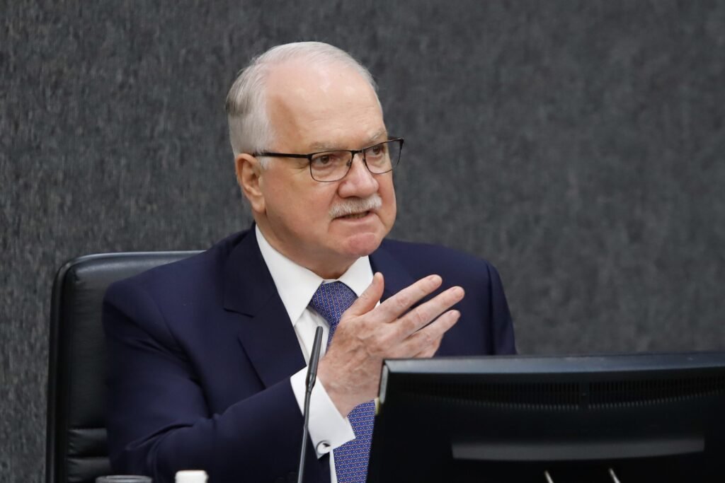 Uma decisão aprovada sem um único voto contrário pode mudar, de forma silenciosa, quanto se paga acima do teto no serviço público — e o efeito real só aparece quando os números entram em cena. Mas o que exatamente foi aprovado? Foi uma **resolução conjunta do CNJ** que regulamenta as novas regras para os chamados **penduricalhos** na magistratura. A aprovação foi **por unanimidade**, em votação no plenário virtual, acompanhando a proposta apresentada pelo presidente do colegiado, **ministro Luiz Edson Fachin**. Só que isso, por si só, não explica por que o tema ganhou tanto peso. Então por que essa aprovação chama tanta atenção? Porque ela não surge isolada. O ato segue uma **determinação do STF**, que atribuiu ao **CNJ** e ao **CNMP** a tarefa de operacionalizar a limitação desses pagamentos. E é justamente aí que muita gente se surpreende: ao mesmo tempo em que fala em limitação, a decisão, na prática, **permite pagamentos de até 70% além do teto constitucional**. Mas quanto isso representa de verdade? Hoje, o **teto constitucional** está em **R$ 46.366,19**. Com a autorização extrateto, a remuneração pode chegar a **R$ 78.822,52**. A diferença possível é de **R$ 32.456,33**, considerando o teto válido em 2026. Parece um detalhe técnico? Não é. Porque quando se define um percentual desse tamanho, o debate deixa de ser apenas jurídico e passa a ser também fiscal e político. E quando isso começou a valer? As medidas **entraram em vigor em abril**. A votação do texto no CNJ foi submetida na **terça-feira, 7 de abril**, e concluída na **quinta-feira, 9 de abril**. Dos **15 conselheiros**, **11 votaram**, já que **4 cargos estão vagos**. Mas há um ponto que quase passa despercebido: o fato de a aprovação ter sido unânime não elimina a controvérsia sobre o impacto prático da regra. Quem sustentou a base dessa mudança? Na condição de **decano do STF**, **Gilmar Mendes** fez a leitura do voto conjunto dos quatro relatores que tratam de processos sobre penduricalhos: **Cristiano Zanin**, **Flávio Dino**, **Alexandre de Moraes** e o próprio contexto consolidado pela Corte. Só que a pergunta inevitável vem logo depois: se existe um limite de 70% além do teto, isso vale para tudo? Não. E é aqui que o assunto fica ainda mais sensível. **Não entram nesse limite** os pagamentos feitos como **auxílio saúde** em caso de procedimento hospitalar com reembolso. Também ficam fora do cálculo o **13º salário**, o **adicional de férias**, o **abono de permanência de caráter previdenciário** e a **gratificação mensal por acúmulo de funções eleitorais**. Ou seja, o limite existe, mas não alcança todos os itens que podem compor a remuneração. Então a medida reduz gastos ou apenas reorganiza o que pode ser pago? O que se sabe, com base no que foi informado, é que o **STF** afirma que o limite imposto aos penduricalhos e ao **quinquênio** pode gerar uma **economia de R$ 7,3 bilhões por ano**. Só que o dado seguinte muda a leitura de tudo: ainda assim, devem ser gastos cerca de **R$ 7,4 bilhões anuais** com esses benefícios. De onde vem essa dimensão bilionária? Um estudo intitulado **“Benchmark internacional sobre teto salarial no setor público”**, produzido pela **República.org** e pelo **Movimento Pessoas à Frente**, com dados compilados entre agosto de 2024 e julho de 2025, indica que as carreiras do **Judiciário** e do **Ministério Público** receberam **R$ 14,7 bilhões em pagamentos acima do teto** em um ano. O que acontece depois dessa comparação muda o foco do debate: a questão já não é apenas se haverá corte, mas quanto continuará sendo pago mesmo após a nova regra. E afinal, qual é o ponto principal dessa aprovação? O **CNJ** aprovou, por unanimidade, o ato que **regulamenta** os penduricalhos conforme a orientação do **STF**, consolidando uma regra que, na prática, **permite remuneração de até 70% acima do teto constitucional**, com exceções relevantes fora desse limite. A promessa é de redução de despesas, mas os próprios números mostram que o volume de pagamentos extrateto continuará bilionário — e é justamente esse contraste que mantém o tema longe de um desfecho simples.