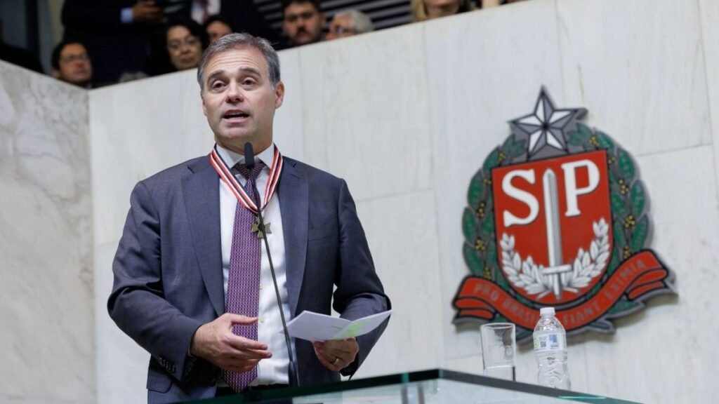 Bastou uma homenagem pública para **André Mendonça** transformar o palco em uma resposta direta às pressões que cercam seu nome. Mas por que um discurso em tom solene ganhou peso político e jurídico tão imediato? Porque o ministro do **STF** é hoje relator de investigações que ocupam o centro do debate nacional, entre elas o caso do **Banco Master** e as apurações sobre **fraudes no INSS**, processos marcados por suspeitas bilionárias e por personagens influentes. E o que exatamente ele quis sinalizar sem entrar nos detalhes dos autos? Ao falar na **Assembleia Legislativa de São Paulo**, na noite de segunda-feira, Mendonça preferiu destacar os princípios que, segundo afirmou, devem orientar sua atuação. Em vez de comentar diretamente os processos, usou a cerimônia para reforçar uma ideia central: suas decisões não podem ser guiadas por amizade, conveniência ou pressão externa. Qual foi a mensagem mais direta nesse sentido? Ela apareceu quando o ministro tratou de **imparcialidade**. “**Imparcialidade é olhar para todos de forma igual. É não privilegiar amigos e não perseguir inimigos. Eu não tenho esse direito**”, afirmou. A declaração veio em meio a críticas sobre possíveis influências em sua atuação e funcionou como resposta pública a esse ambiente de desconfiança. Mas por que essas palavras repercutem tanto agora? Porque os casos sob sua relatoria envolvem investigações de grande impacto. No caso do **Banco Master**, há a possibilidade de novos desdobramentos com uma eventual delação. Já nas investigações sobre **fraudes no INSS**, o peso político e financeiro das apurações também amplia a atenção sobre cada movimento do relator. Nesse cenário, qualquer manifestação do ministro passa a ser lida como sinal sobre a forma como pretende conduzir decisões futuras. E ele falou apenas de imparcialidade? Não. Mendonça também abordou a ideia de **integridade**, resumida por uma frase que guiou sua fala: **“fazer o certo pelo motivo certo”**. O que ele quis dizer com isso? Que a atuação de um magistrado, segundo suas palavras, não deve ser movida por busca de reconhecimento nem por cálculo de conveniência. Foi nesse ponto que ele acrescentou outra observação: “**Às vezes, fazer o certo não traz aplauso. Pelo contrário, pode trazer crítica. Ainda assim, é isso que precisa ser feito**”. Como essa visão se conecta ao papel que ele exerce no Supremo? O próprio ministro respondeu ao falar sobre sua chegada ao gabinete e sobre a forma como enxerga a função. “**A cadeira não é poder. É dever. E o problema começa quando a gente confunde essas duas coisas**”, declarou. A frase reforçou a tentativa de afastar a ideia de que o posto no tribunal possa ser tratado como espaço de prestígio pessoal, e não como responsabilidade institucional. Houve também recado ao próprio **Judiciário**? Sim. Em meio ao aumento da cobrança pública sobre decisões da Corte, Mendonça afirmou que magistrados não estão imunes a críticas. Mas fez uma ressalva importante: precisam estar imunes a atitudes que comprometam a **credibilidade da Justiça**. Foi nesse contexto que disse: “**Nós não estamos imunes a críticas, mas precisamos estar imunes a atitudes que comprometam a credibilidade da Justiça. Nem tudo que é permitido convém para quem ocupa essa função**”. Quem acompanhou essa fala de perto? A cerimônia reuniu nomes de peso da política ligados ao campo da direita, como o governador de São Paulo, **Tarcísio de Freitas**, o prefeito da capital, **Ricardo Nunes**, e o ministro da **AGU**, **Jorge Messias**. E houve ainda uma menção que chamou atenção: durante o evento, Mendonça citou Messias e manifestou o desejo de vê-lo futuramente no **STF**. O discurso ficou restrito ao ambiente institucional? Não completamente. Em meio às declarações sobre dever, integridade e imparcialidade, o ministro também mencionou sua trajetória pessoal. **Natural de Santos** e com raízes em **Miracatu**, ele trouxe referências à própria origem durante a fala. E quais foram, afinal, os recados deixados por André Mendonça naquela noite? Que sua atuação nos casos do **Banco Master** e das **fraudes no INSS** será, segundo afirmou, guiada por **imparcialidade**, por **integridade** e pela noção de que a função no **STF** representa **dever**, não **poder**. Em suas palavras: **“Imparcialidade é olhar para todos de forma igual. É não privilegiar amigos e não perseguir inimigos. Eu não tenho esse direito”**, **“fazer o certo pelo motivo certo”**, **“Às vezes, fazer o certo não traz aplauso. Pelo contrário, pode trazer crítica. Ainda assim, é isso que precisa ser feito”**, **“A cadeira não é poder. É dever. E o problema começa quando a gente confunde essas duas coisas”** e **“Nós não estamos imunes a críticas, mas precisamos estar imunes a atitudes que comprometam a credibilidade da Justiça. Nem tudo que é permitido convém para quem ocupa essa função”**.