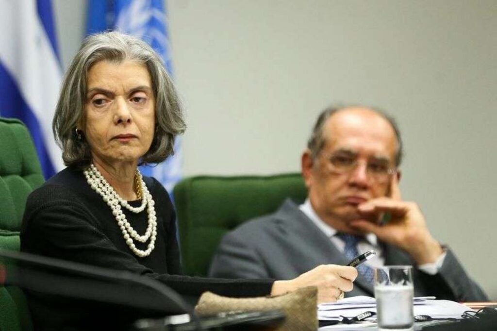 Ela saiu antes da hora, e isso acendeu uma pergunta que Brasília inteira começou a fazer no mesmo instante: por quê? A resposta mais imediata parece simples, mas será que é só isso? Oficialmente, a ministra Cármen Lúcia anunciou que deixará antecipadamente a presidência do Tribunal Superior Eleitoral, mesmo com o mandato previsto para terminar apenas em 3 de julho. Se a saída já tem explicação, então por que a decisão chamou tanta atenção? Porque o movimento altera diretamente o calendário interno da Corte. E quando um cronograma muda no TSE, a dúvida surge quase automaticamente: quem ganha tempo com isso? A resposta aponta para o ministro Nunes Marques, indicado para assumir a presidência e, com a mudança, ter um período maior para conduzir os preparativos do pleito. Mas se esse é o motivo, por que tanta gente viu algo além da justificativa formal? É aí que o caso começa a ficar mais sensível. Cármen Lúcia afirmou que, se permanecesse até o fim do mandato, seu sucessor teria cerca de 100 dias para estruturar todo o processo eleitoral. Em outras palavras, a antecipação permitiria uma transição mais ampla e uma preparação mais confortável. Parece razoável. Mas há um detalhe que quase ninguém percebe de imediato: a decisão veio logo depois de críticas duras e públicas. Críticas de quem? Do ministro Gilmar Mendes. E é aqui que a maioria se surpreende, porque o debate não foi genérico nem abstrato. Gilmar criticou a morosidade no andamento de processos na corte eleitoral, citando diretamente o caso do ex-governador Cláudio Castro. Se a crítica foi tão direta, o que exatamente estava em jogo? O ponto central era o tempo de tramitação. O processo começou em 2022, na primeira instância, mas só começou a ser julgado no TSE em novembro do ano passado. O desfecho veio apenas em março, depois de dois pedidos de vista e do recesso do Judiciário. Isso abriu espaço para uma cobrança incômoda: por que temas com impacto político tão alto demoram tanto para avançar? Cármen Lúcia respondeu a essa pressão? Sim, e de forma objetiva. Ela argumentou que, sempre que os processos são liberados para julgamento pelos relatores, eles são prontamente incluídos na pauta. A explicação tenta delimitar responsabilidades. Mas isso encerrou a discussão? Nem de longe. O que aconteceu depois muda tudo, porque Gilmar Mendes não parou nesse ponto. Em tom crítico, ele ainda lembrou de outra ação pendente no TSE, desta vez envolvendo o governador de Roraima, Antônio Denarium, que também corre o risco de ser cassado. E quando um ministro amplia a crítica para além de um caso específico, a leitura muda: já não se trata apenas de um processo, mas de um sinal de insatisfação com o ritmo da Corte. Então a desistência antecipada foi consequência direta dessas críticas? Não há confirmação disso. E esse é justamente o ponto mais delicado. O provável motivo revelado não aparece como uma confissão, mas como uma combinação de fatores que se encaixam no tempo: de um lado, a justificativa institucional de dar mais prazo ao sucessor; de outro, o desgaste provocado por cobranças públicas sobre a lentidão de julgamentos sensíveis. Mas por que isso importa tanto agora? Porque o TSE não lida apenas com prazos burocráticos. Ele lida com a organização do processo eleitoral, com decisões que podem afetar mandatos e com a pressão permanente por respostas rápidas em casos de grande repercussão. Quando a presidência muda antes do previsto, a leitura política e institucional se impõe. E qual é, afinal, o provável motivo por trás da desistência? Tudo indica que a saída antecipada foi apresentada como uma medida para ampliar o tempo de preparação de Nunes Marques para o pleito, mas ganhou outro peso por ter ocorrido logo após as críticas de Gilmar Mendes à morosidade da Corte. A explicação oficial existe, mas o contexto tornou impossível ignorar o que estava ao redor. Só que há uma última pergunta que continua no ar: a antecipação resolve apenas um problema de calendário ou também tenta reduzir a pressão sobre uma gestão já colocada sob questionamento? É essa dúvida, mais do que a saída em si, que mantém o caso aberto.