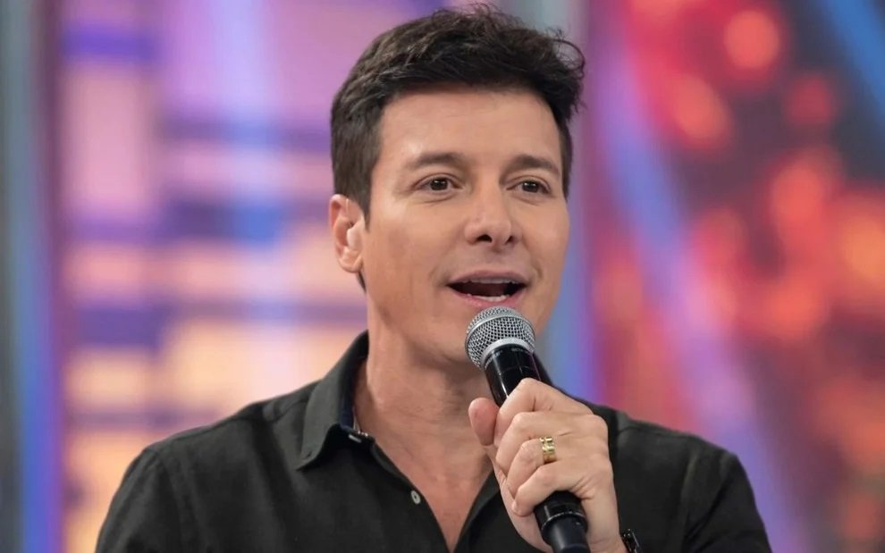 Uma mudança de rota coloca **Rodrigo Faro** diante de um projeto inédito e abre uma nova fase na televisão e no streaming brasileiro. Mas o que torna esse anúncio tão chamativo? A resposta começa pelo encontro entre um nome já conhecido do público e um formato que ainda não teve versão no país. Qual é esse novo trabalho? Faro vai comandar **Herança em Jogo**, novo reality original do **Globoplay**, com gravações previstas para maio. A novidade não chama atenção apenas por marcar a chegada do apresentador à plataforma, mas também porque envolve um jogo em que **inteligência** e **estratégia** conduzem cada decisão. E por que esse reality desperta tanta curiosidade? Porque ele é apresentado como a primeira adaptação internacional de **The Inheritance**, formato distribuído pela **All3Media International** e adquirido pela **Globo**. A versão brasileira será exclusiva do Globoplay e terá produção da **Formata**, levando para o público nacional um reality psicológico criado pela **Studio Lambert**. Mas qual será exatamente o papel de Rodrigo Faro nessa dinâmica? Ele assumirá a função de **testamenteiro**, personagem central na condução do jogo. Será dele a responsabilidade de acompanhar o andamento da disputa e garantir que cada linha do que foi documentado seja cumprida. Isso dá ao apresentador uma posição decisiva dentro da narrativa do programa, conectando sua presença à própria lógica da competição. E como o próprio Faro define essa estreia? Em declaração divulgada sobre o projeto, ele afirmou: “Estou muito feliz com a minha chegada ao **Globoplay** em um reality que vai mexer com a cabeça de todo mundo! Em **Herança em Jogo**, a manipulação e a estratégia ditam as regras. Como testamenteiro, meu papel é garantir que cada linha do que foi documentado seja honrada, mas confesso: o que mais me intriga é ver até onde os participantes serão capazes de ir para conquistar esse jogo”. Essa escolha surpreende? Em parte, sim, mas ela também faz sentido quando se observa a trajetória do apresentador. Por quê? Porque Rodrigo Faro reúne mais de **quatro décadas de carreira** na televisão brasileira, com passagens pela dramaturgia e pelo entretenimento. Essa combinação ajuda a explicar sua presença em um formato que exige condução, leitura de jogo e relação direta com o público. Onde essa trajetória começou a ganhar força? Na atuação, com participações em novelas conhecidas como **A Indomada** (1997), **Malhação** (1998), **Suave Veneno** (1999), **O Cravo e a Rosa** (2000-2001), **A Padroeira** (2001-2002) e **Chocolate com Pimenta** (2003-2004), entre outros trabalhos. Esses títulos ajudaram a consolidar sua imagem antes de uma virada importante na carreira. E quando Faro se firmou como apresentador de realities e programas de auditório? Isso aconteceu ao longo dos anos em atrações como **Ídolos** (2008-2011), **O Melhor do Brasil** (2008-2014), **A Fazenda de Verão** (2012), **Canta Comigo** (2021-2024) e **Hora do Faro** (2014 a 2024). Esse histórico mostra familiaridade com formatos de competição e convivência com a tensão típica de programas guiados por desempenho, emoção e expectativa. Então, o que fica claro com esse novo passo? Que Rodrigo Faro chega ao Globoplay para liderar um projeto que une **reality psicológico**, disputa estratégica e um formato ainda inédito no Brasil. As gravações começam em maio, a produção será da Formata, a criação original é da Studio Lambert, e o nome dessa nova aposta é **Herança em Jogo**.