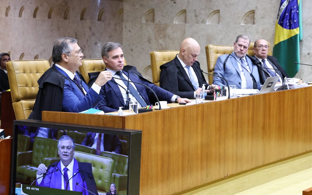 Parecia apenas mais um recurso técnico, mas o que o Supremo decidiu agora mexe com um tema que volta e meia incendeia o debate público: quem pode, de fato, tentar mudar o alcance de uma decisão já tomada? A resposta começa por um ponto que muita gente ignora. O que estava em julgamento não era exatamente o indulto em si. Então por que o caso voltou à pauta? Porque houve uma tentativa de rediscutir os efeitos da decisão anterior, ampliando a forma como ela poderia ser aplicada em outros casos. E é justamente aí que a história fica mais delicada. Mas se o mérito já tinha sido analisado antes, o que ainda restava discutir? Restava saber se quem apresentou o recurso tinha autorização jurídica para fazer isso. Parece detalhe? Parece. Só que esse detalhe quase sempre define o resultado. Antes mesmo de se falar sobre o conteúdo do pedido, o Supremo precisou enfrentar uma pergunta anterior: a entidade que recorreu podia recorrer? E por que isso importa tanto? Porque, no Judiciário, não basta discordar de uma decisão. É preciso ter legitimidade para contestá-la naquele tipo específico de processo. Sem isso, o tribunal nem entra no mérito do que está sendo pedido. O que acontece depois muda tudo, porque a discussão deixa de ser sobre o indulto e passa a ser sobre quem tem voz formal para tentar alterar a decisão. Foi exatamente esse o entendimento que formou maioria. O Supremo rejeitou o recurso apresentado pela Ordem dos Advogados do Brasil e manteve a validade do indulto natalino editado em 2022 pelo então presidente Jair Bolsonaro. A medida concede perdão a condenados por crimes cuja pena máxima não ultrapassa cinco anos. Mas há um ponto que surpreende muita gente: a Corte não voltou a declarar o decreto constitucional agora, porque isso já havia sido definido antes. Então o que a OAB queria, afinal? Queria ampliar o alcance da decisão e detalhar critérios para a aplicação do benefício em outros casos. Em outras palavras, buscava uma formulação mais precisa sobre como o entendimento do Supremo deveria repercutir além daquele processo. Parece uma discussão restrita? Talvez. Mas é justamente desse tipo de ajuste que podem surgir efeitos práticos relevantes. E por que o pedido não avançou? Porque a maioria dos ministros entendeu que a OAB, nesse caso, atuava como amicus curiae, uma espécie de colaboradora do processo. E é aqui que a maioria se surpreende: nessa condição, segundo o entendimento adotado, a entidade não pode apresentar recurso em ações com repercussão geral. Ou seja, o obstáculo não foi o conteúdo do que ela defendia, mas a posição processual que ocupava. Quem sustentou esse entendimento? O relator do caso, ministro Flávio Dino. Ele votou para não conhecer o recurso e também defendeu a manutenção da redação original da tese fixada pelo Supremo. Para Dino, o entendimento já expressa de forma suficiente os fundamentos que levaram à validação do indulto. Acompanharam esse voto Alexandre de Moraes, Cristiano Zanin, Dias Toffoli, Edson Fachin e Cármen Lúcia, formando maioria no plenário virtual. Mas o julgamento terminou? Ainda não completamente. A análise segue aberta até segunda-feira, 13. Isso muda a maioria já formada? Até aqui, não. O cenário consolidado é o de rejeição do recurso e manutenção do indulto. Só que existe um detalhe que mantém o tema vivo: mesmo quando a decisão parece definida, o debate sobre os limites de atuação de entidades em processos de repercussão geral continua tendo peso muito além deste caso. E por que isso continua chamando atenção? Porque a decisão não trata apenas de um decreto assinado em 2022. Ela também reforça como o Supremo enxerga o papel de quem participa de ações relevantes sem ser parte principal nelas. No fim, o ponto central não foi apenas Bolsonaro, nem apenas o indulto, mas a fronteira entre participar e poder recorrer. E essa fronteira, agora reafirmada, ainda deve provocar novas discussões.