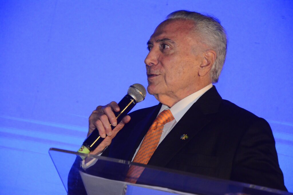 Uma ligação mudou o rumo de uma proposta que já parecia definida. Mas o que, de fato, Michel Temer disse ter articulado nos bastidores para transformar a discussão sobre **anistia** em uma saída baseada na **dosimetria das penas**? Segundo o ex-presidente, a mudança começou a ganhar forma depois de uma entrevista ao **Roda Viva**, da **TV Cultura**. E por que esse momento foi decisivo? Porque, de acordo com Temer, dois dias após essa fala, o presidente da Câmara, **Hugo Motta**, ligou para ele com a intenção de “desenterrar” um texto nessa linha. A ideia já não seria mais insistir em uma anistia “**ampla, geral e irrestrita**”, mas trabalhar uma proposta de **redução de penas**. E quem entraria nessa articulação a partir daí? Temer afirmou que **Paulinho da Força**, anunciado como relator, e o deputado **Aécio Neves** o procuraram depois desse contato inicial. O que ele sugeriu? Que o texto não avançasse sem conversa com o **Supremo Tribunal Federal**. Na avaliação dele, aprovar uma medida sem esse diálogo abriria caminho para uma reação da Corte. Mas por que Temer considerava essa conversa com o Supremo indispensável? Porque, nas palavras dele, sem um entendimento prévio, o risco era simples: o Congresso produziria um ato e o **STF** poderia derrubá-lo depois. Por isso, ele relatou ter orientado que a construção fosse feita “de comum acordo”. E o que aconteceu em seguida? Ainda segundo Temer, os envolvidos entraram em contato com o Supremo e acabaram aprovando essa nova **dosimetria**. Se a proposta foi aprovada, por que o tema continua em disputa? Porque o presidente **Lula** vetou o texto. E esse veto encerrou a discussão? Não. Temer afirmou que agora o veto está até para ser derrubado no **Congresso Nacional**. O que falta para isso acontecer? O agendamento de uma sessão conjunta pelo presidente do Congresso, senador **Davi Alcolumbre**. E por que essa etapa ainda não ocorreu? De acordo com membros da oposição citados na reportagem, Alcolumbre estaria usando o veto à dosimetria como **moeda de troca**. Em troca de quê? Com vistas a não pautar um pedido de instauração de uma **Comissão Parlamentar Mista de Inquérito**, a **CPMI sobre o Banco Master**. A entrevista de Temer ficou restrita à articulação sobre penas? Não. Ele também falou sobre a relação entre os poderes. O que disse? Que há uma **desarmonia entre os poderes** e que isso seria, em sua visão, uma **inconstitucionalidade** por si só. Por quê? Porque, segundo ele, essa desarmonia surge quando “as pessoas saem do seu **quadrado constitucional**”. E o que Temer entende como saída para esse cenário? Na avaliação dele, para haver **segurança jurídica**, cada poder precisa cumprir suas próprias funções e permanecer dentro de seus limites constitucionais. O que decorreria disso? Ainda segundo o ex-presidente, a segurança jurídica levaria à **segurança social** e à **crença nas instituições estatais**. E qual é o diagnóstico que ele faz hoje? O de que existe **descrença nas instituições estatais**. Em que contexto essa fala acontece? Em meio à **crise de credibilidade do STF** e à tensão com os demais poderes. O que agravou esse ambiente? A atuação do ministro **Flávio Dino** sobre temas ligados ao dinheiro das instituições, ao tratar ao mesmo tempo das **emendas parlamentares** e das **verbas indenizatórias** que ficam fora do teto de gastos, os chamados **penduricalhos**. E houve alguma tentativa de mediação nesse quadro? Sim. A segunda medida levou o presidente da Corte, ministro **Edson Fachin**, a conduzir uma reunião de mediação entre as cúpulas. Qual foi o resultado? Uma **regra de transição**. Há ainda outro dado que amplia o peso político da fala de Temer? Há. Foi ele quem levou **Alexandre de Moraes** ao cargo de ministro do Supremo. E por que isso chama atenção agora? Porque Moraes, ex-ministro da Justiça de Temer, condenou o ex-presidente **Jair Bolsonaro** a **27 anos e três meses de prisão**. Além disso, conduz uma tentativa de **extradição**, da Itália, do ex-assessor **Eduardo Tagliaferro**, e também recebe críticas pela condução do caso do ex-assessor **Filipe Martins**. No centro de tudo, o relato de Temer sobre a articulação ficou resumido em uma orientação direta: **“Vocês precisam conversar com o Supremo, porque vocês produzem um ato aqui sem o diálogo com o Supremo, vai acontecer o seguinte: o Supremo vai derrubar, tem que ser uma coisa de comum acordo”.** Segundo ele, depois disso, houve contato com o **STF**, a nova **dosimetria** foi aprovada, **Lula vetou**, e a eventual derrubada desse veto agora depende de uma sessão conjunta a ser marcada por **Davi Alcolumbre**.