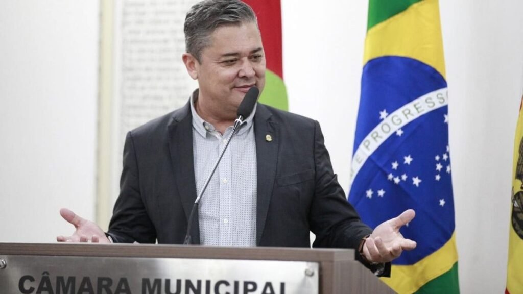 Quando tudo parecia caminhar para uma definição, o relógio virou peça central e empurrou o desfecho mais uma vez para frente. Mas por que um novo prazo muda tanto um caso que já vinha sendo acompanhado de perto? Porque, em processos assim, tempo não é só calendário: tempo pode alterar estratégia, reorganizar argumentos e, principalmente, influenciar o que será considerado na reta final. E foi exatamente isso que aconteceu agora, com a concessão de mais 10 dias para a defesa se manifestar. Só que essa decisão não surgiu do nada. O que justificou esse novo prazo? O ponto decisivo foi o aparecimento de novas provas depois da notificação feita à defesa, ainda no início de março. Se surgem novos elementos no meio do caminho, a lógica do processo exige que a parte investigada tenha a chance de responder. Parece um detalhe técnico, mas é justamente esse tipo de detalhe que pode redefinir o ritmo de tudo. E por que isso chama tanta atenção? Porque o caso não trata apenas de uma investigação comum. Há uma comissão processante em andamento, e ela não está discutindo diretamente a culpa criminal, mas algo que pode ser igualmente devastador no campo político: a possível quebra de decoro parlamentar. E é aqui que muita gente se surpreende: mesmo separado das investigações criminais, esse processo pode levar à perda do mandato. Então estamos falando de duas frentes diferentes? Exatamente. De um lado, seguem as apurações criminais conduzidas pelo Ministério Público e pela Polícia Civil, envolvendo suspeitas de rachadinha, lavagem de dinheiro e corrupção. De outro, a Câmara analisa se a conduta do vereador fere o decoro parlamentar. São caminhos distintos, embora nasçam do mesmo caso e avancem ao mesmo tempo. Mas há um ponto que quase passa despercebido: se o processo político é separado do criminal, por que as novas provas pesam tanto? Porque a comissão precisa formar convicção com base no que foi reunido até aqui, e qualquer novo material pode reforçar, enfraquecer ou redirecionar a análise. Antes de um relatório final, a defesa precisa falar. Sem isso, a etapa seguinte ficaria vulnerável. E quem está no centro dessa disputa? Só depois de tantas camadas o nome aparece com mais clareza: trata-se do vereador Almir Vieira, do PP, em Blumenau. Ele está afastado do cargo desde fevereiro e é alvo de uma investigação da Polícia Civil de Santa Catarina. A operação foi deflagrada no dia 3 de fevereiro, com mandados de busca e apreensão, inclusive no gabinete dele na Câmara. Almir chegou a ser preso em flagrante, mas foi solto horas depois. O que exatamente está sendo investigado? A suspeita principal envolve rachadinha, prática ilegal em que assessores devolvem parte do salário ao político. Além disso, também são apurados possíveis atos de corrupção, lavagem de dinheiro e eventuais desvios de recursos públicos. O que acontece depois disso muda tudo, porque a discussão deixa de ser apenas policial e passa a atingir diretamente a permanência dele no cargo. Mas a Câmara já não tinha se movido antes? Sim. Antes mesmo da formação da comissão processante, os vereadores aprovaram a abertura do processo de cassação no dia 24 de fevereiro, com 10 votos favoráveis em plenário. Isso mostra que o caso já havia ultrapassado a fase da suspeita silenciosa e entrado no terreno da reação institucional. E agora, qual é o próximo passo? Com o novo prazo, a defesa poderá apresentar manifestação e argumentos antes da análise final da comissão. A próxima reunião já tem data marcada: 29 de abril. Até lá, a expectativa gira em torno do que será dito sobre essas novas provas e de como isso pode influenciar o relatório. Mas existe um detalhe que mantém tudo em suspense: a comissão ainda não decide sozinha o destino final. Ela conduz a apuração e elabora um relatório, mas a palavra definitiva caberá ao plenário da Câmara, que vai decidir se houve quebra de decoro e se o mandato deve ou não ser cassado. E é justamente aí que o caso ganha seu ponto mais sensível. O novo prazo não encerra nada. Ele adia, reorganiza e aumenta a tensão sobre o que ainda será revelado — porque, no fim, a pergunta que continua aberta não é apenas o que a defesa vai dizer, mas o peso que isso terá quando os vereadores precisarem votar.